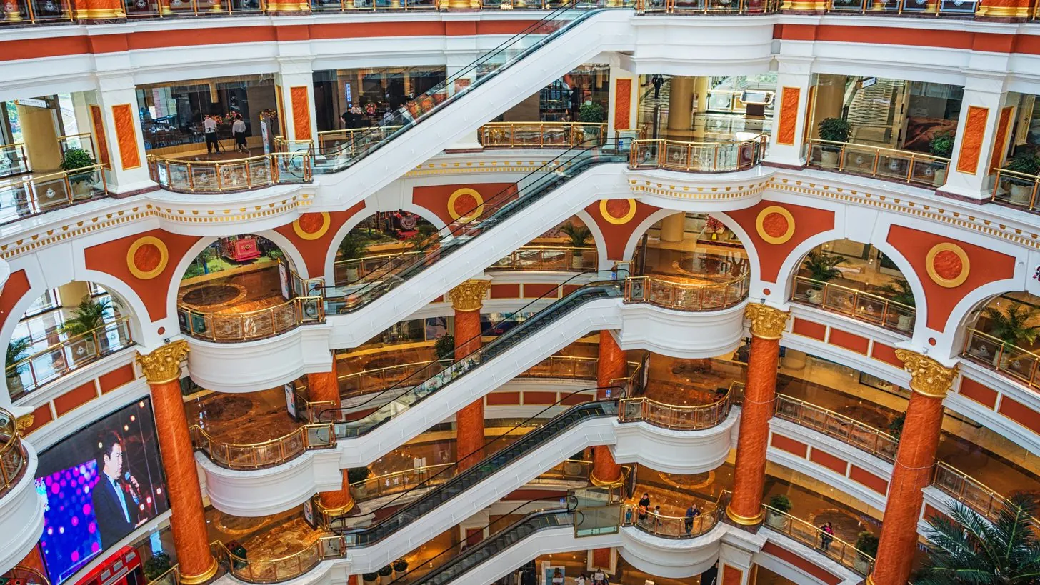 A shopping centre concourse seen from an upper floor, escalators running between levels