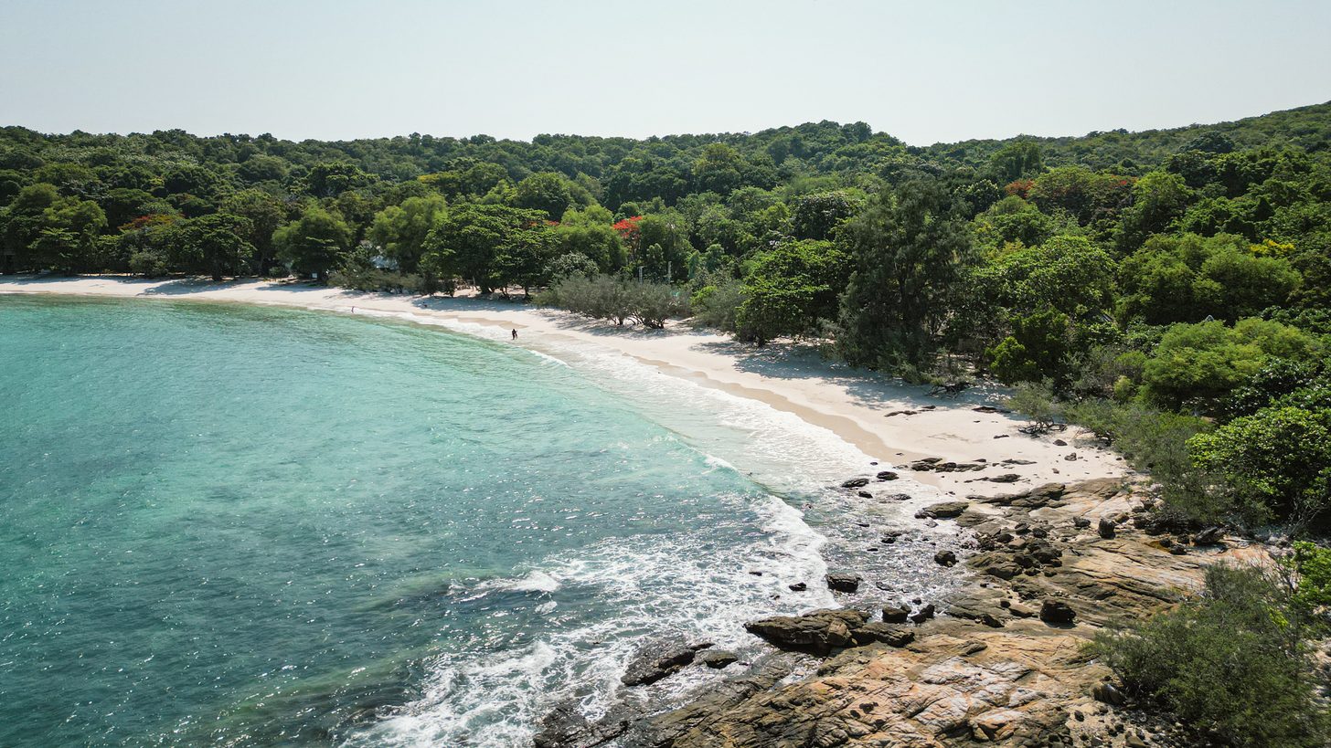 An aerial view of a wooded cove on Koh Samet with pale sand and clear turquoise water