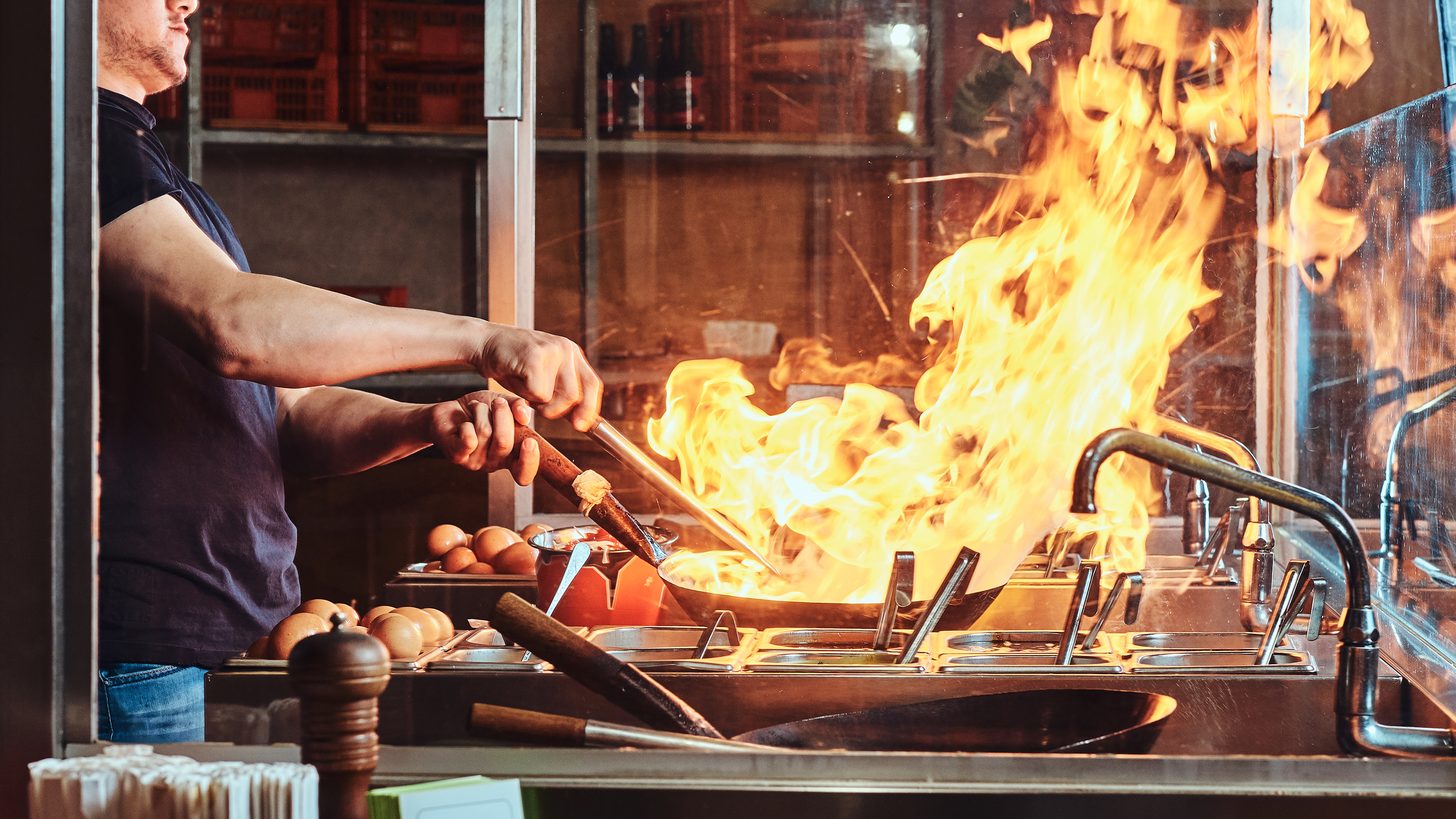 A chef stir-frying in a wok over an open flame