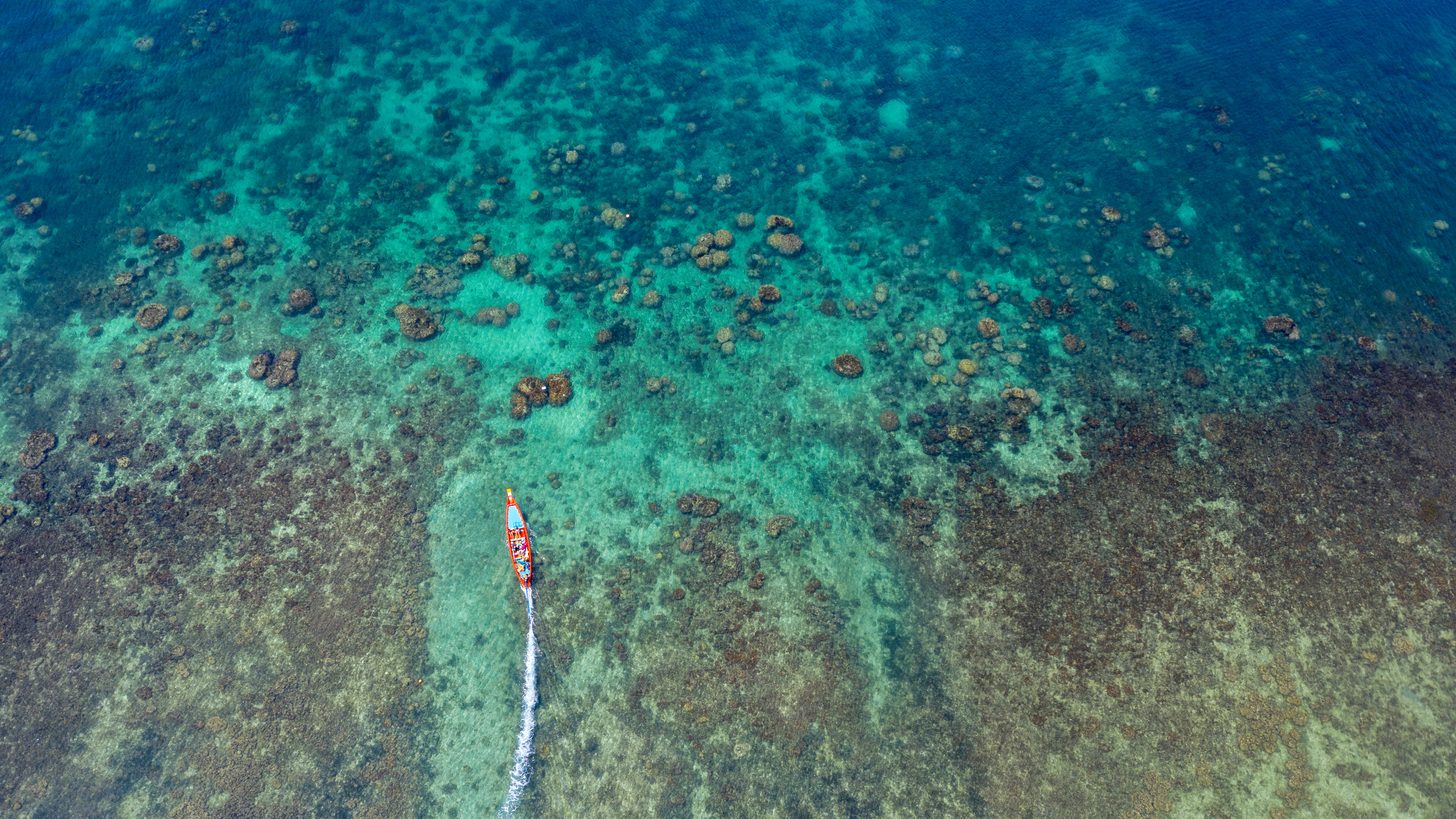 Aerial view of a single longtail boat crossing shallow coral reef in clear water off Koh Tao