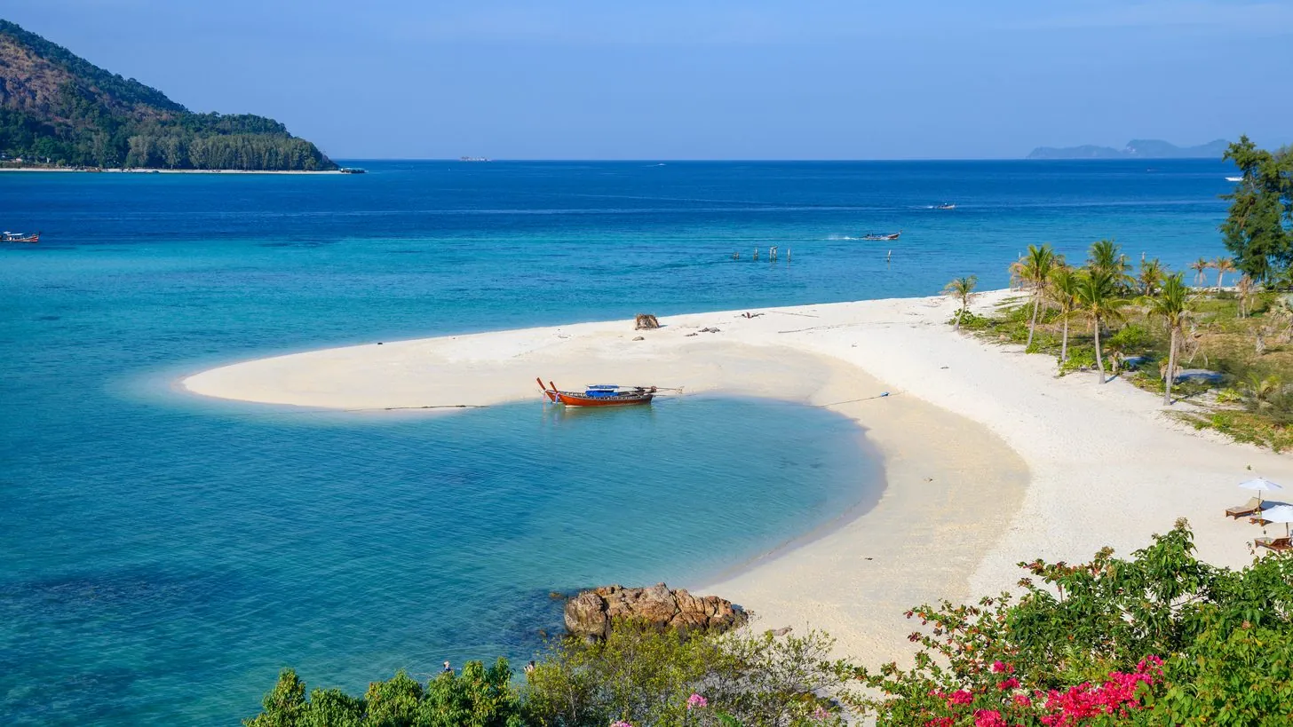 Ein Longtail-Boot an einer weißen Sandbank vor Koh Lipe mit Palmen und klarem flachem Wasser