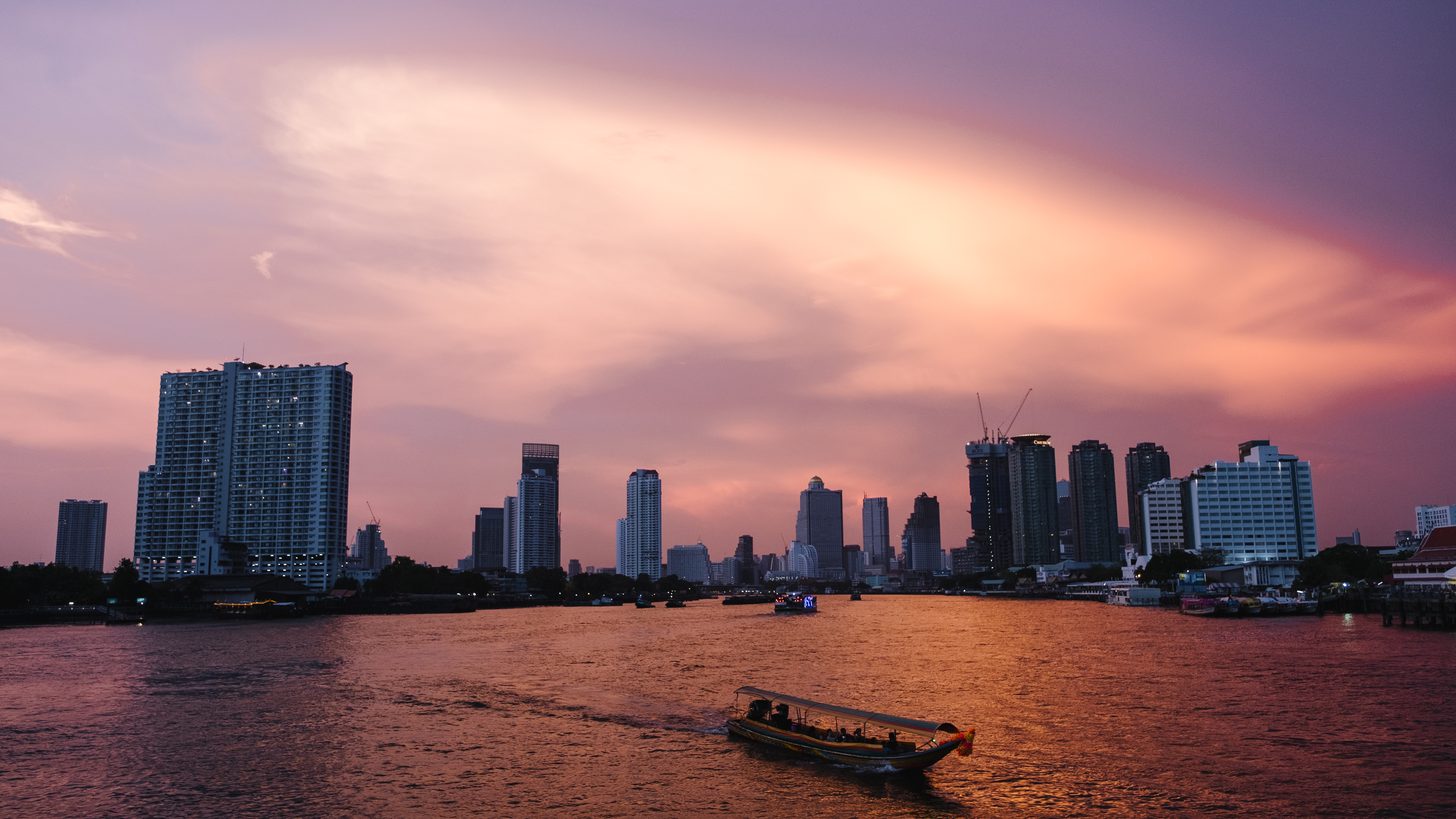 A boat on the Chao Phraya river in Bangkok at sunset with the city skyline behind