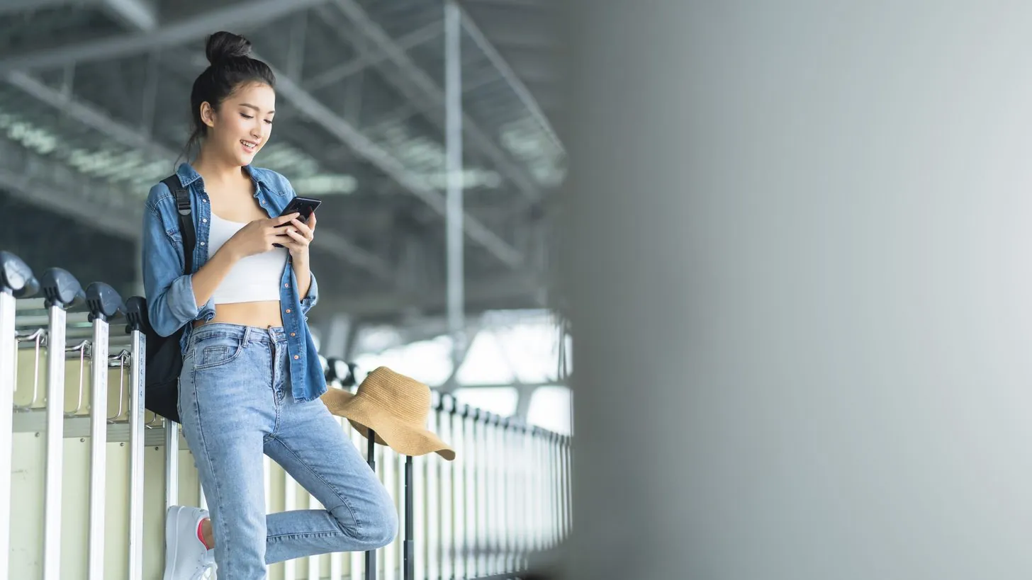 A traveller checking a taxi app on her smartphone at a station platform