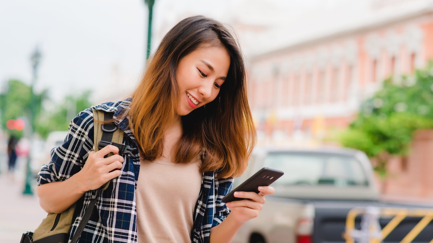A backpacker smiling at her smartphone while travelling in Thailand