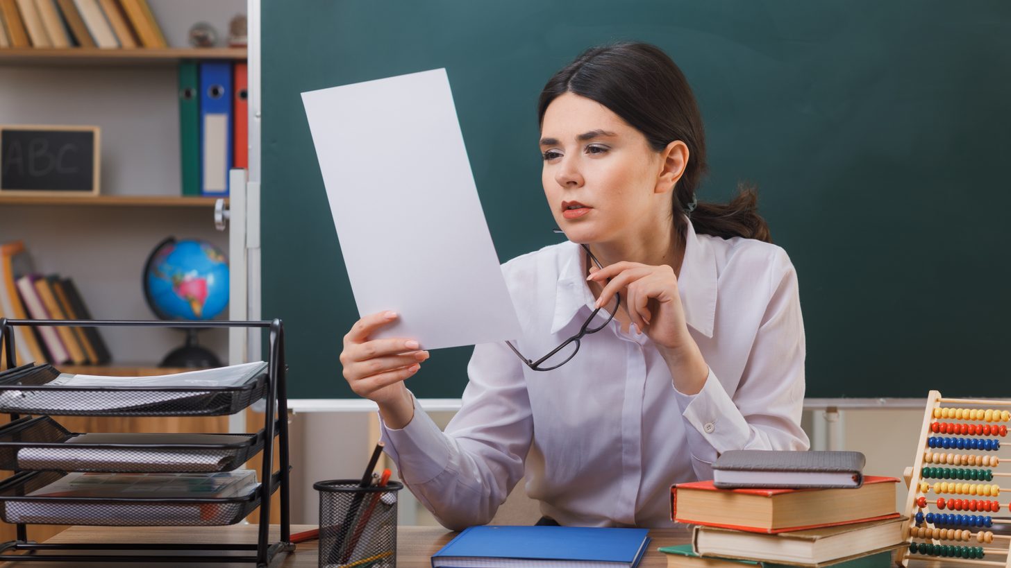 Teacher reviewing a checklist at a classroom desk