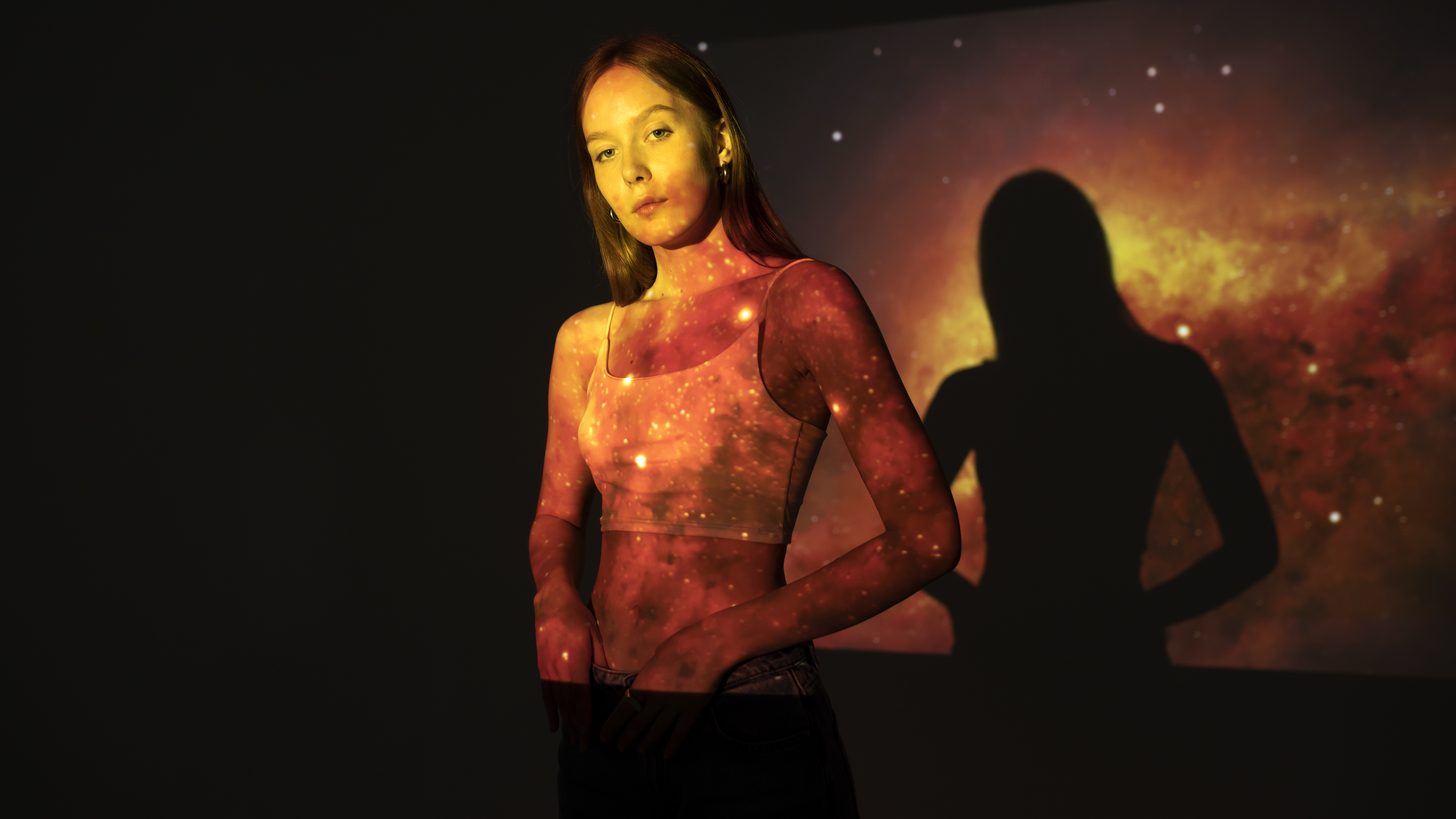 Visitor lit by a swirling galaxy projection in a dark immersive gallery