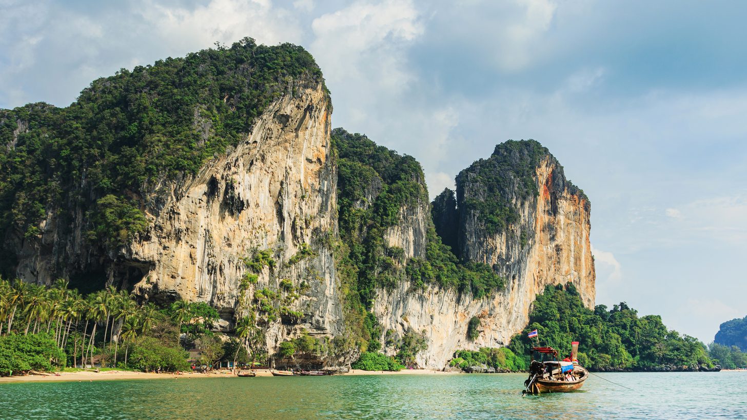 A longtail boat in clear water beneath the limestone cliffs of Railay near Krabi