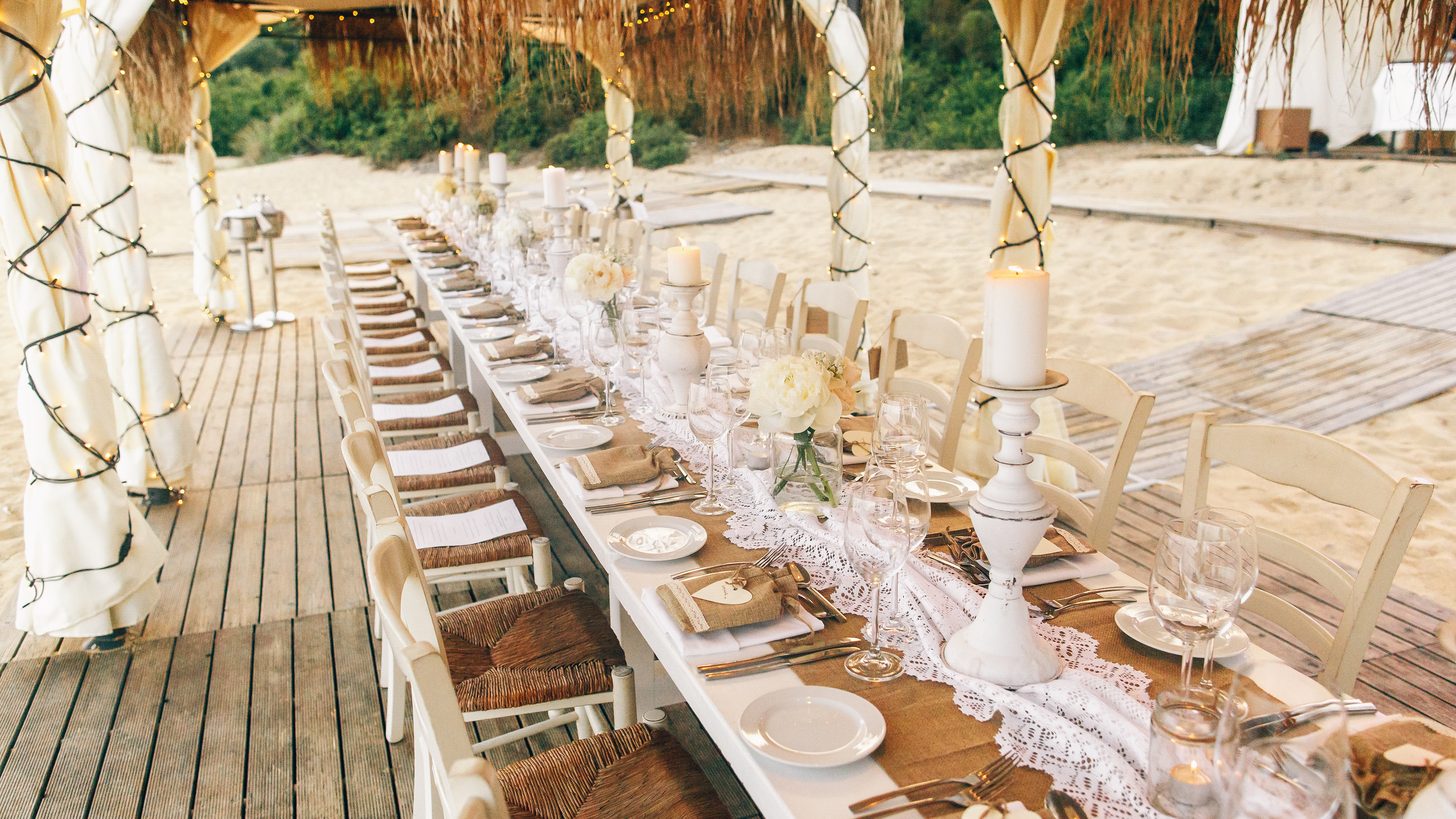 An elegant private dinner table set up on a beach at dusk
