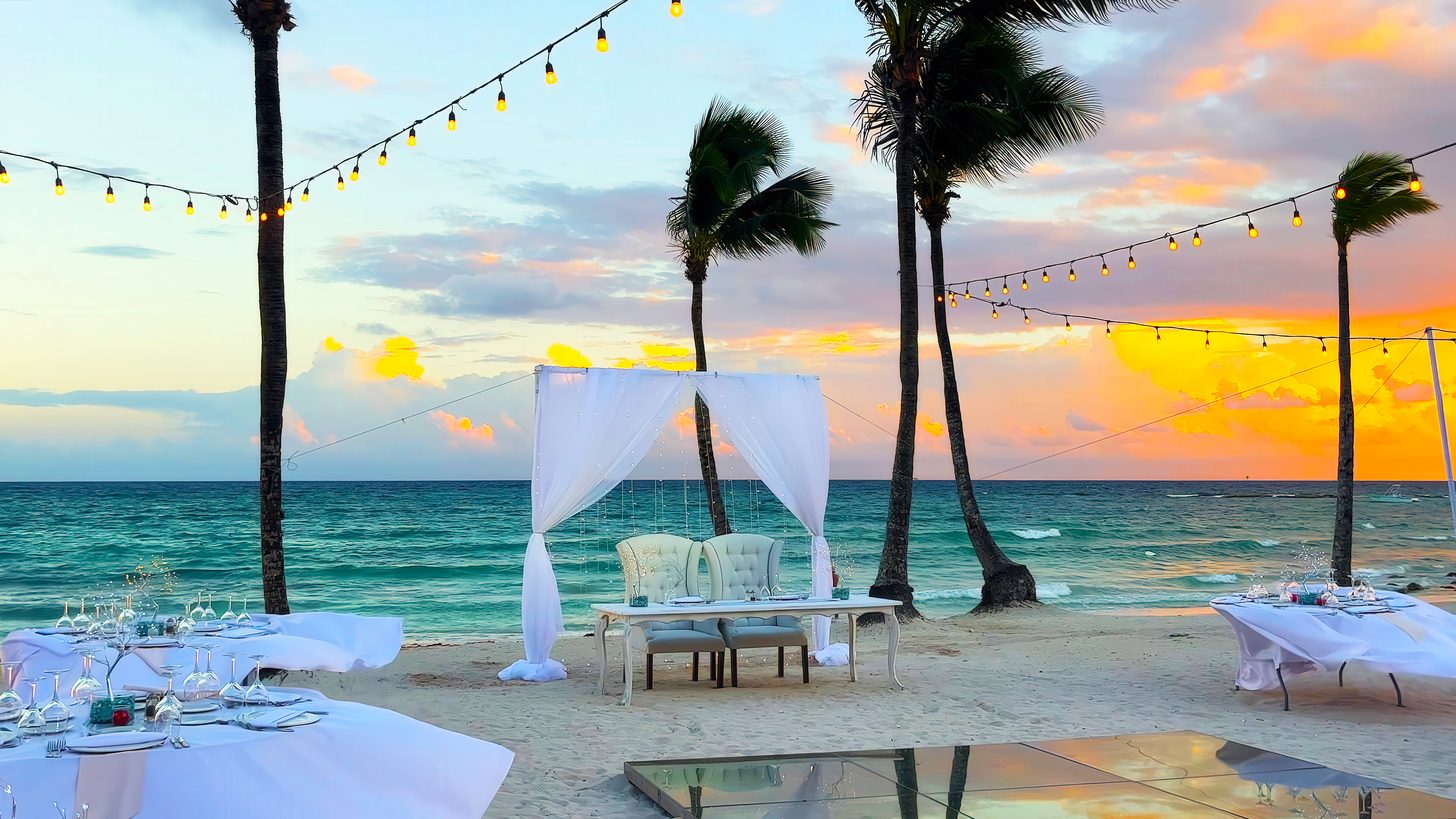 An elegant outdoor beach wedding setup at sunset with an ocean view