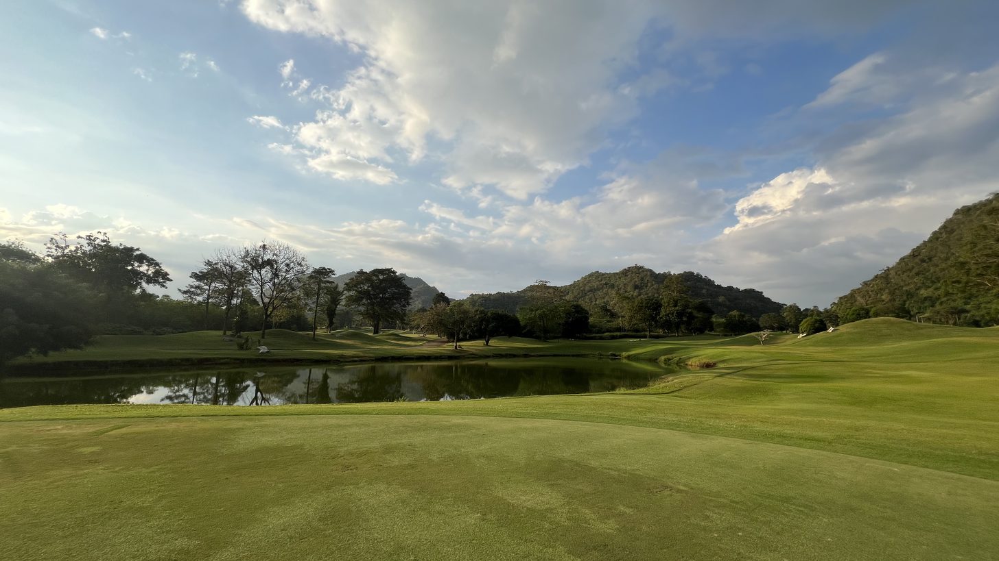 A manicured green with tropical hills in the background