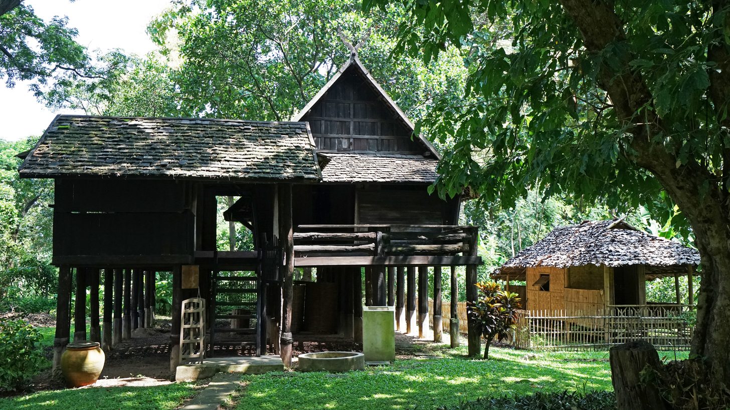 An elevated traditional teak Lanna house against a mountain backdrop