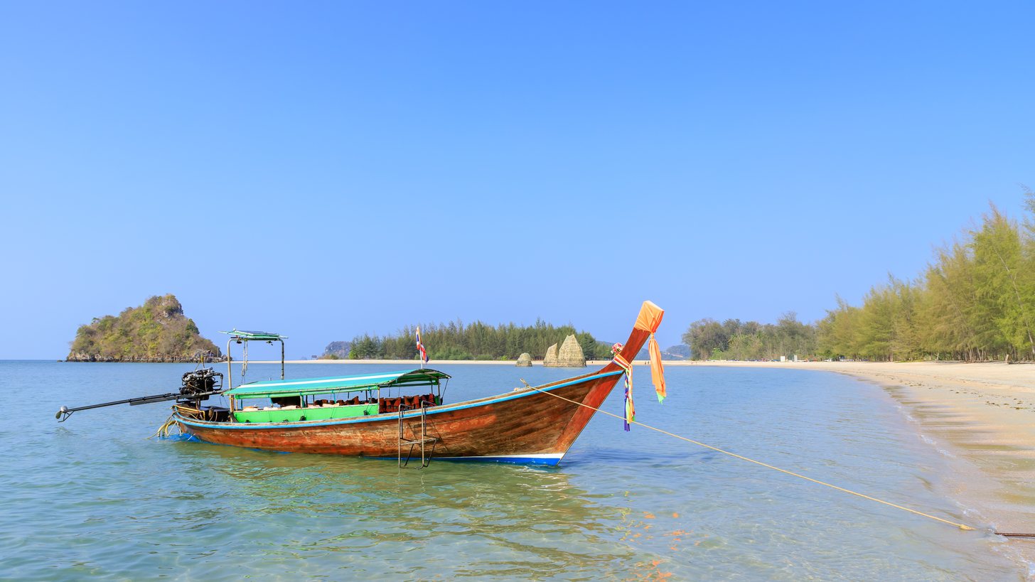A wooden longtail boat moored in shallow turquoise water at Noppharat Thara beach on the Andaman coast near Krabi