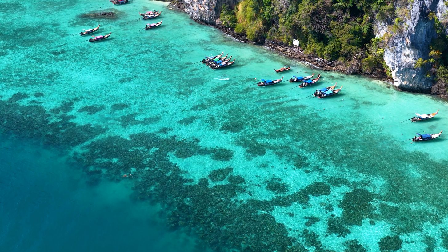 Calm turquoise Andaman sea with longtail boats among limestone cliffs on a clear day
