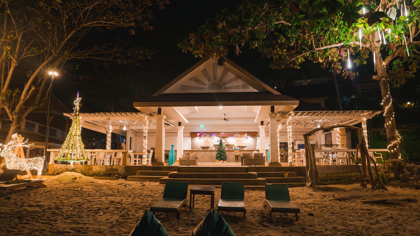 An open-sided beachfront resort pavilion lit for an evening gathering