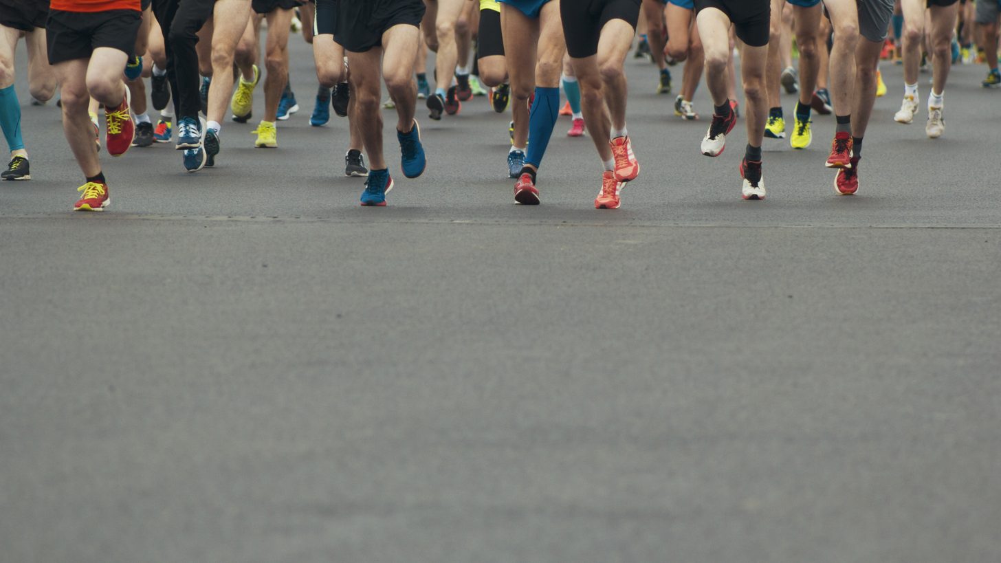Des coureurs franchissant la ligne de départ d’une course sur route à l’aube dans une rue de ville