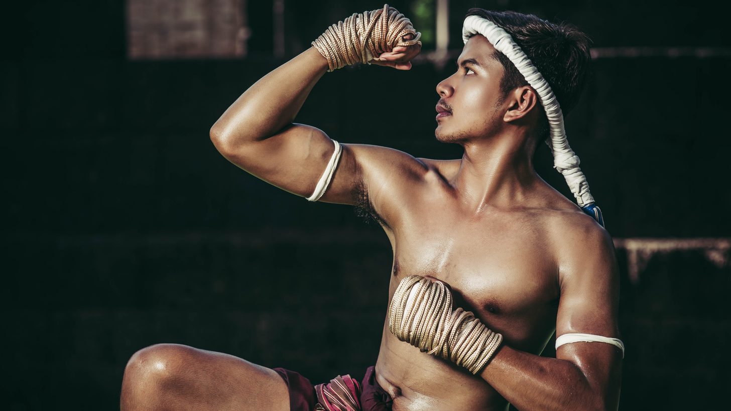 Un pratiquant enroulant ses bandes de mains à côté d’un ring dans une salle de Muay Thai en plein air en Thaïlande