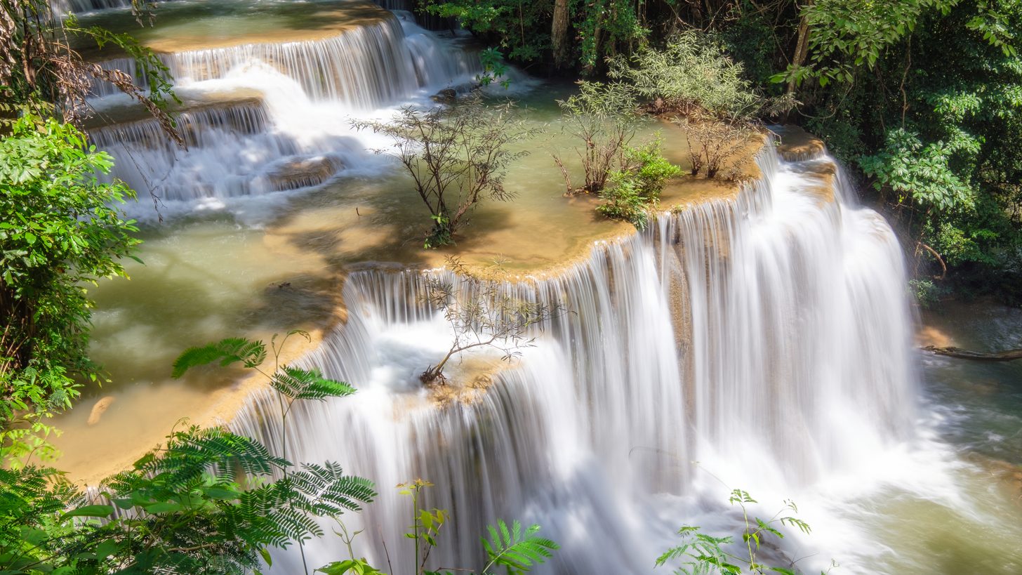 A full waterfall pouring through lush green jungle after seasonal rain in Thailand