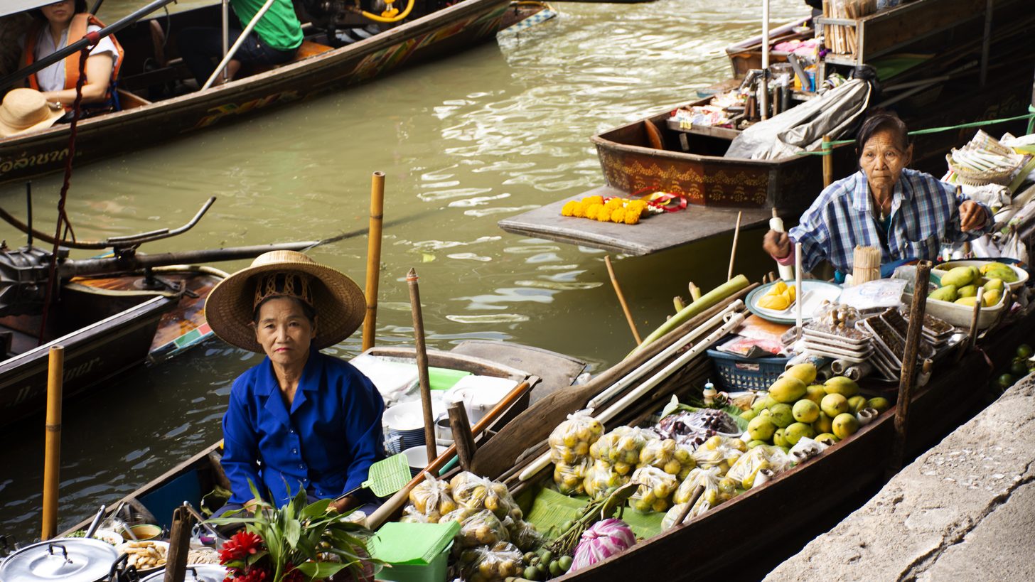 Vendor boats loaded with fruit and souvenirs crowding the main canal junction at Damnoen Saduak floating market, surrounded by visitors