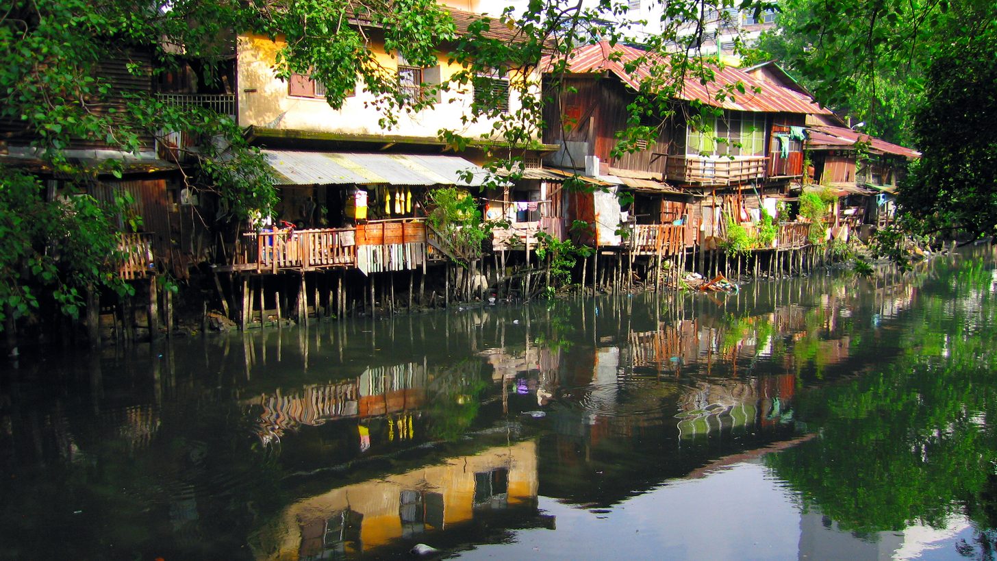 A narrow canal in Ratchaburi lined with wooden stilt houses and small private jetties, with no visitor facilities in sight