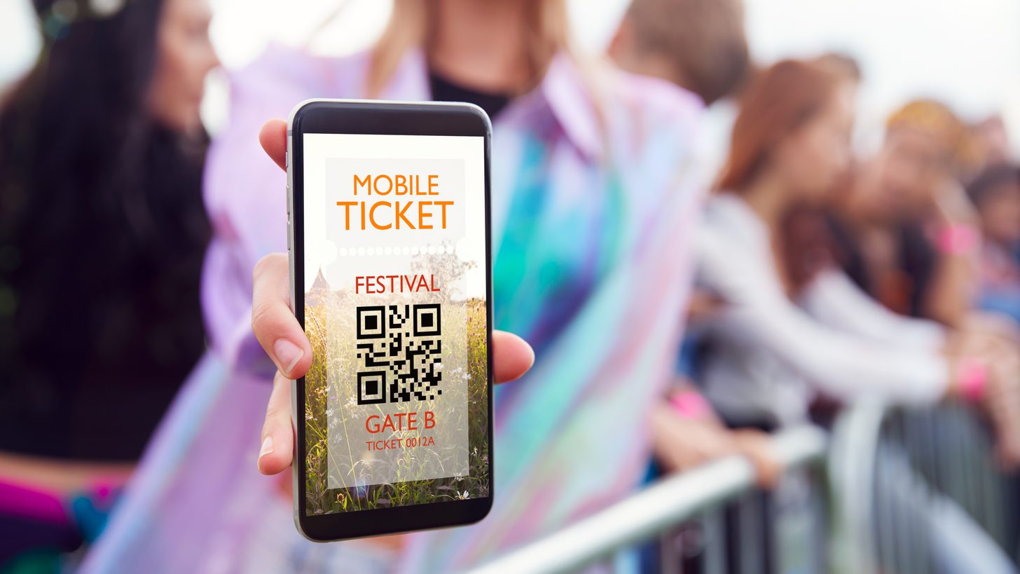 A traveller holding a smartphone screen up to a handheld scanner at the entrance gate of a visitor attraction