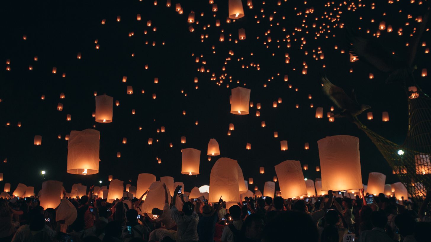 Crowds releasing glowing paper lanterns into the night sky at a festival in northern Thailand