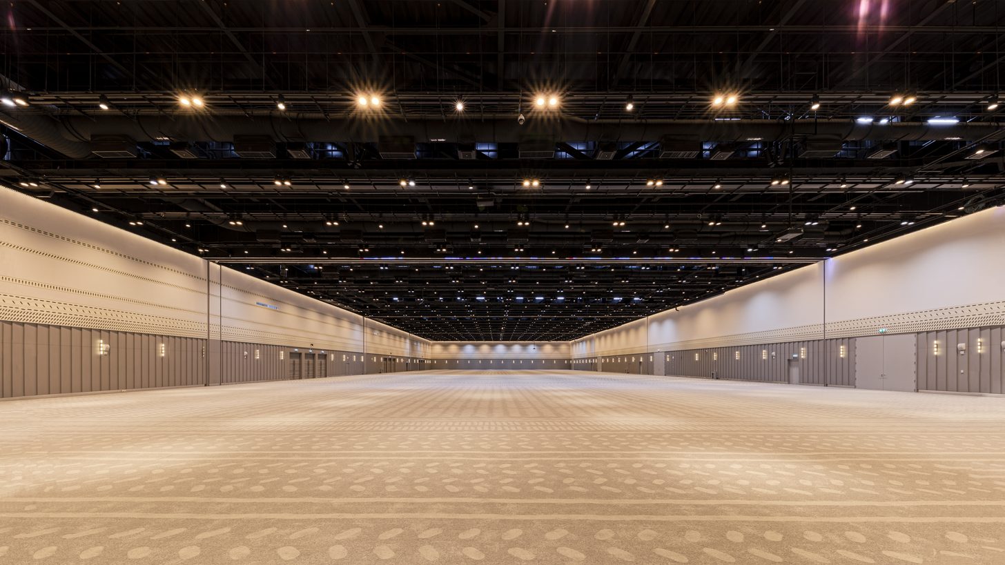 A large empty exhibition hall with a high ceiling and bare floor, waiting for an event build