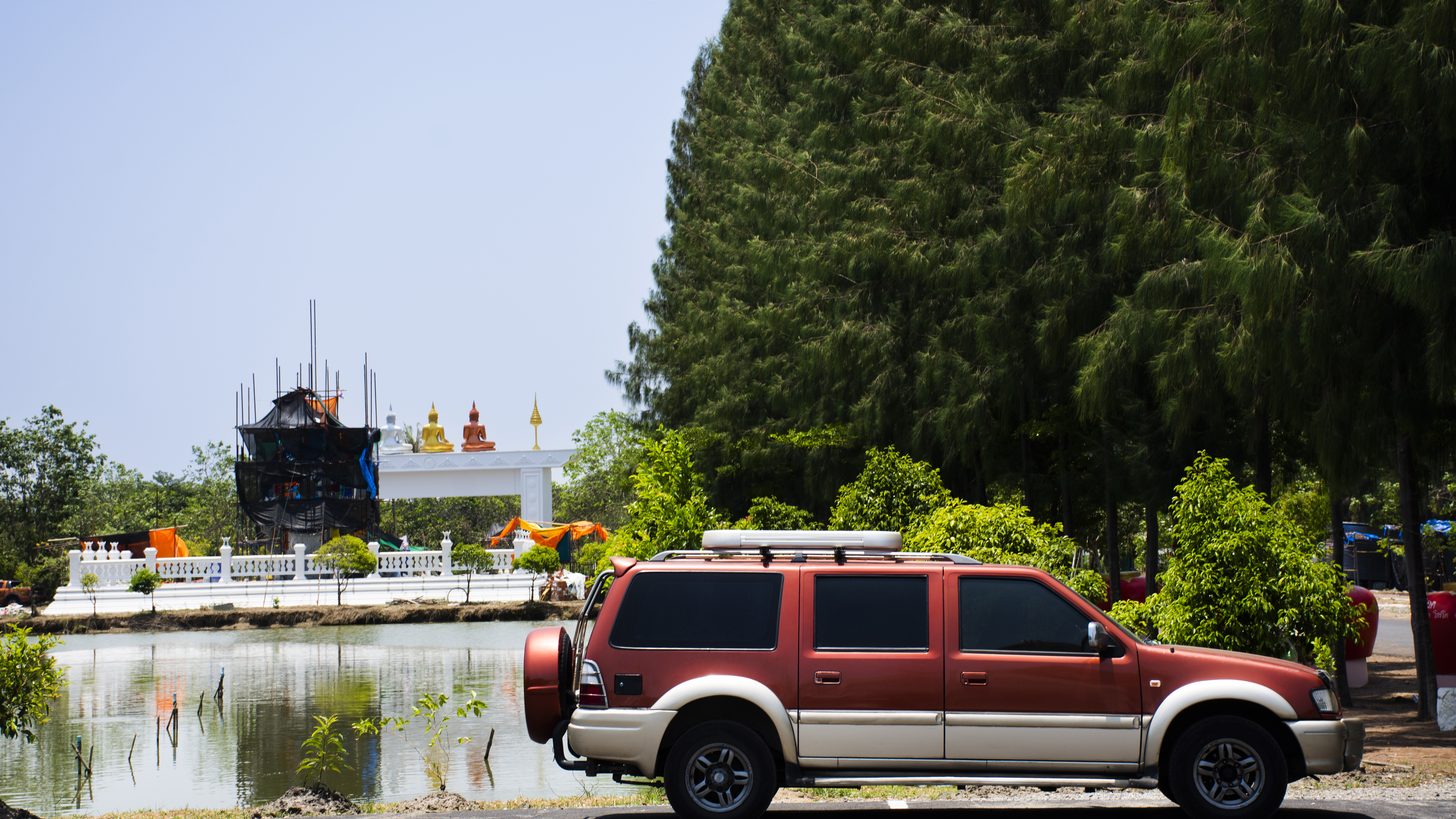 Visitors arriving by car at an inland temple site in Thailand on an overcast morning