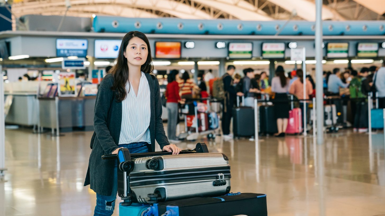 Traveller approaching an airport counter with luggage as others queue behind
