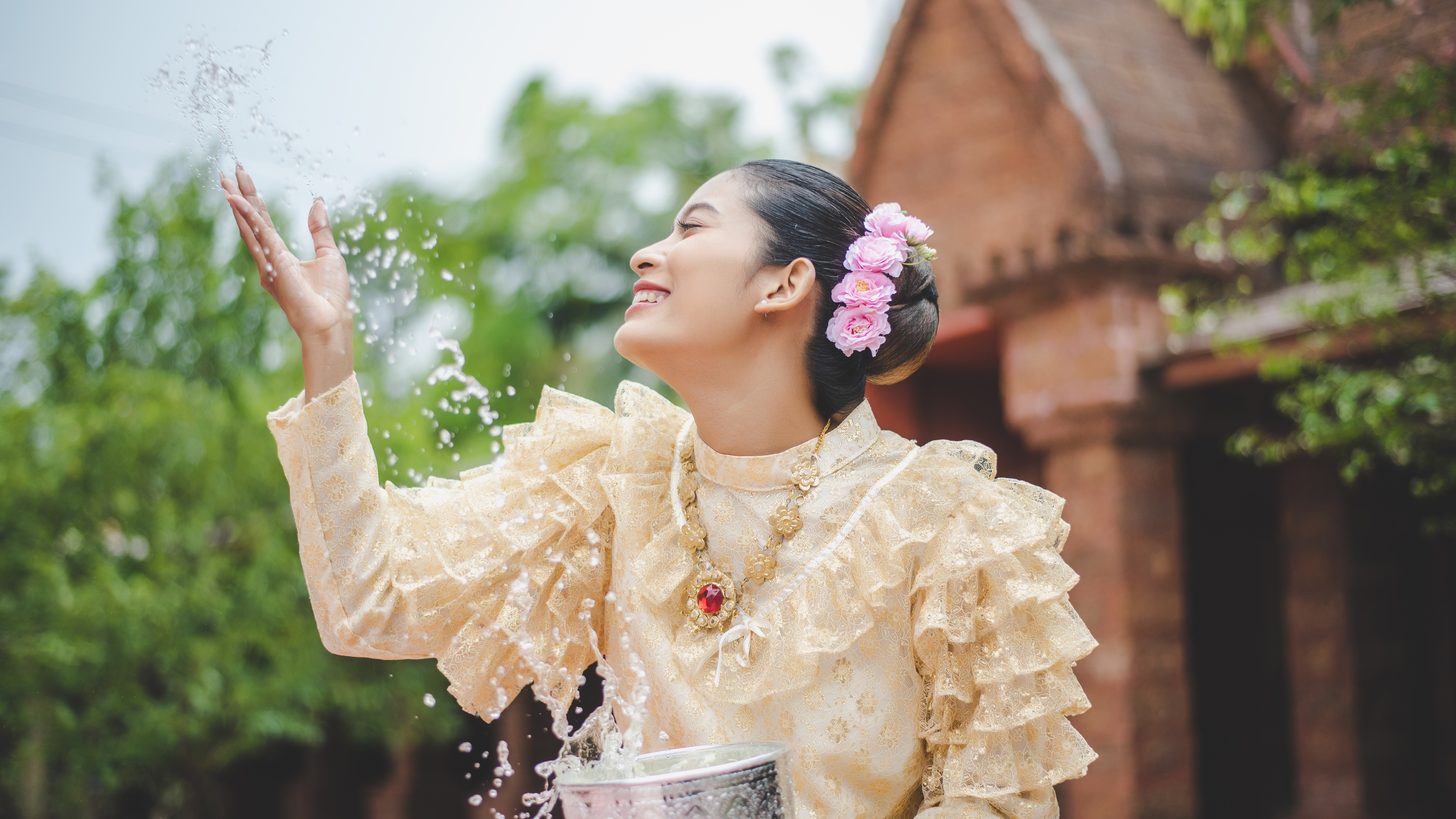 A woman in Thai costume splashing water at a temple during Songkran