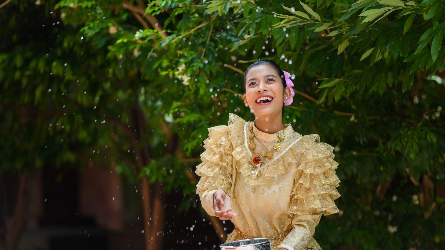 A woman in traditional Thai dress pouring water at a temple during Songkran