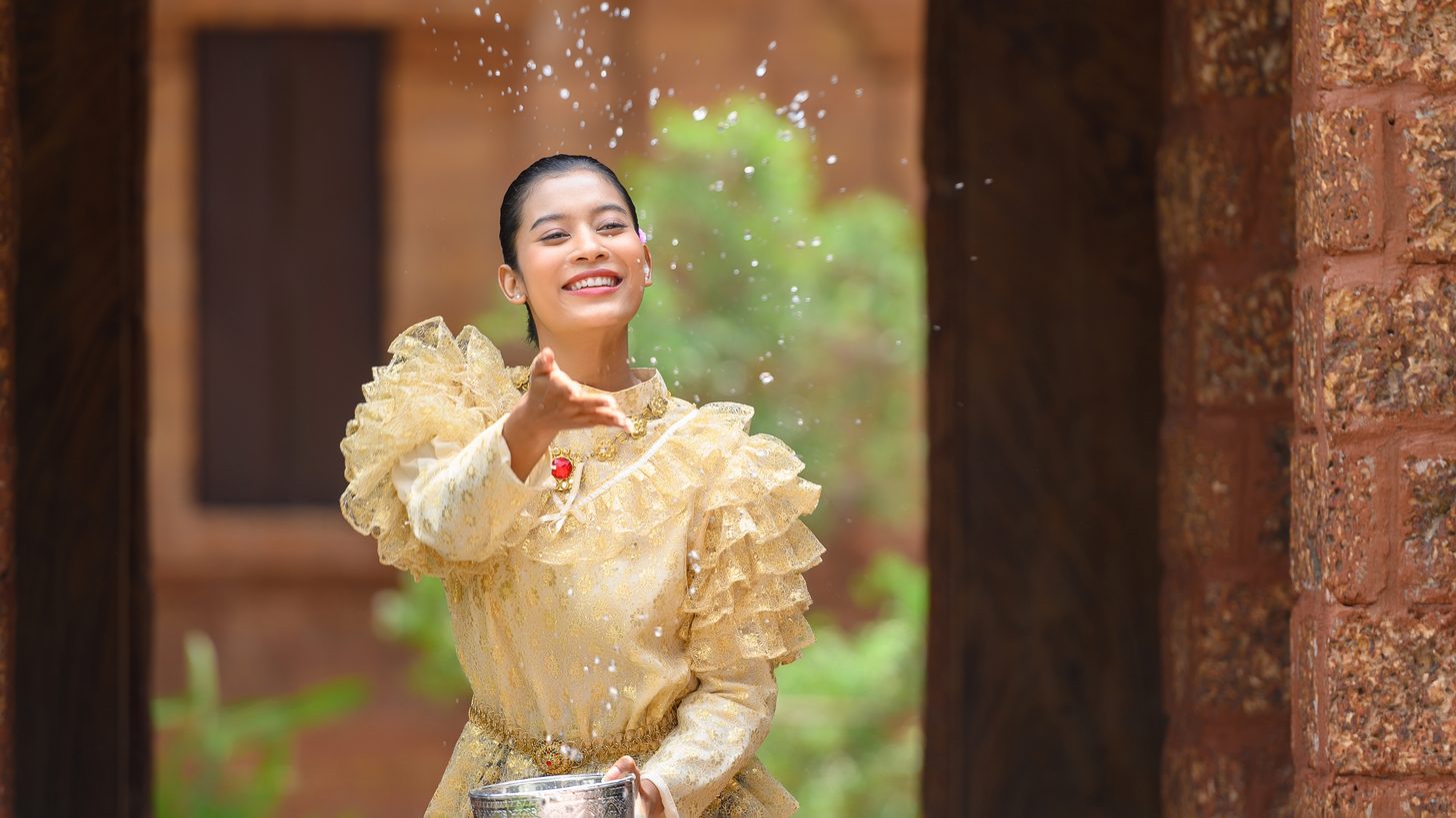 A woman in Thai costume pouring water during a Songkran blessing