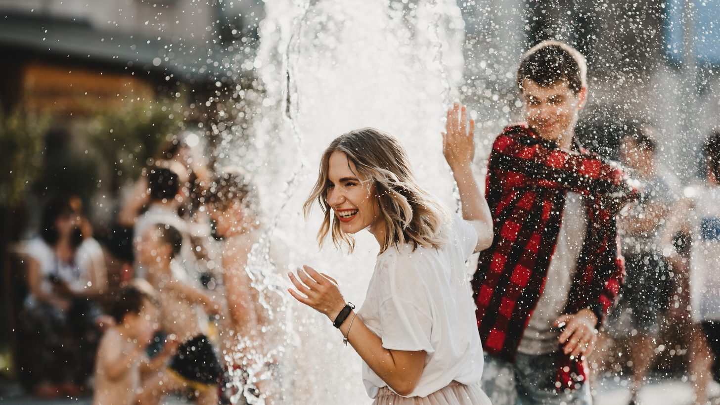 A couple laughing together beside a fountain in the sunshine