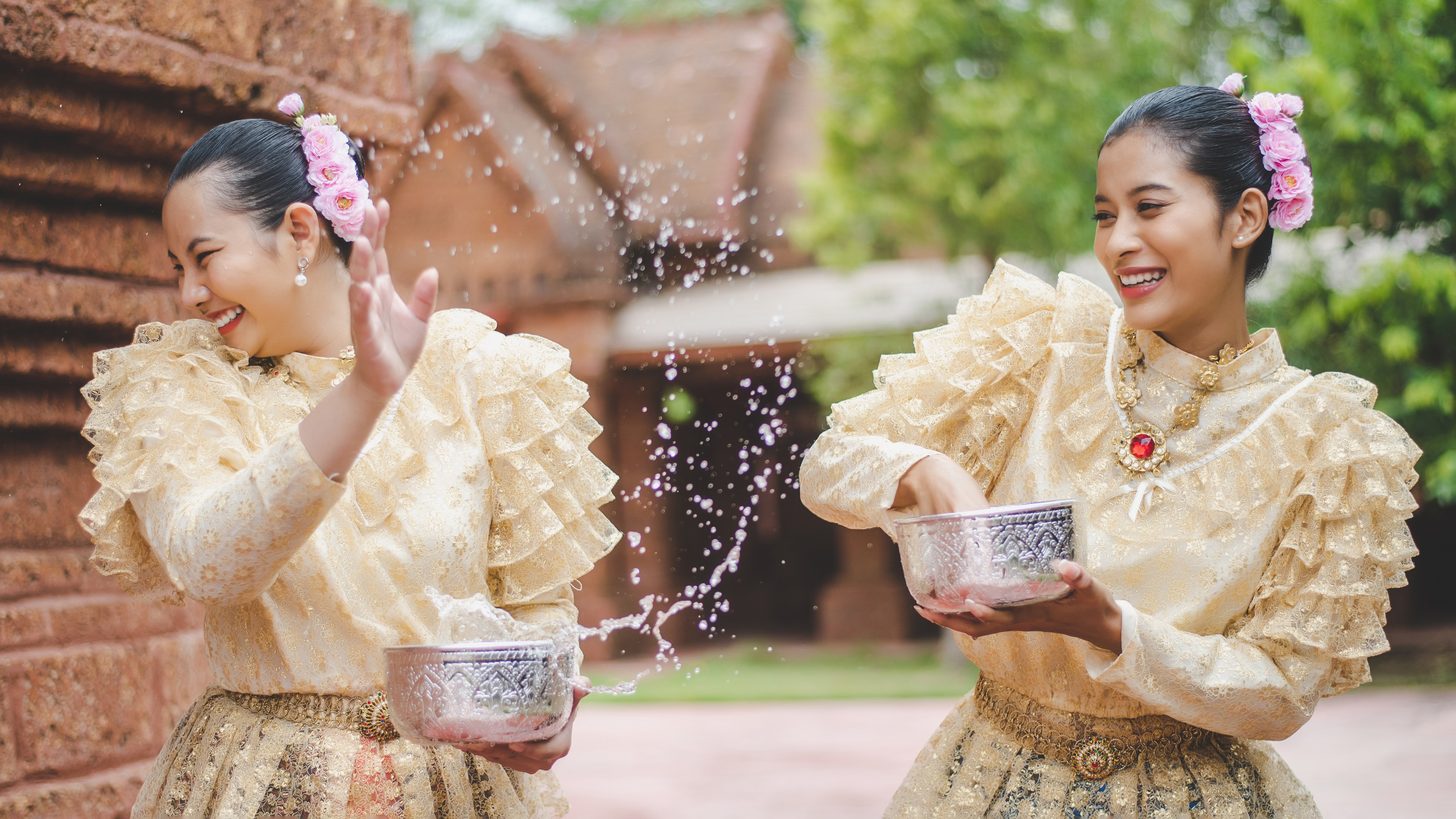 Women in Thai dress pouring water in a Songkran blessing at a temple