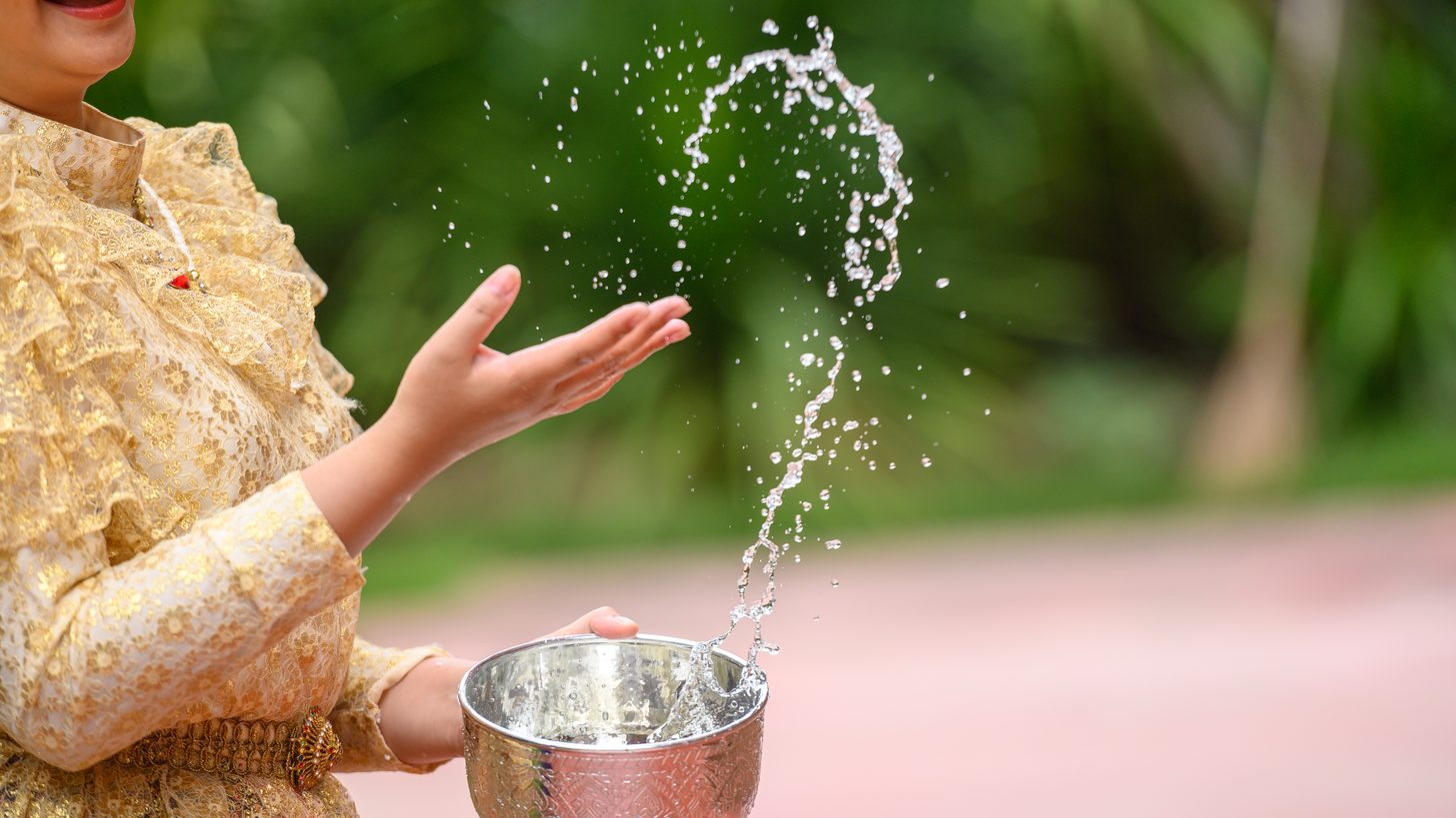 Close-up of hands holding a bowl and pouring water in a Songkran blessing at a Thai temple