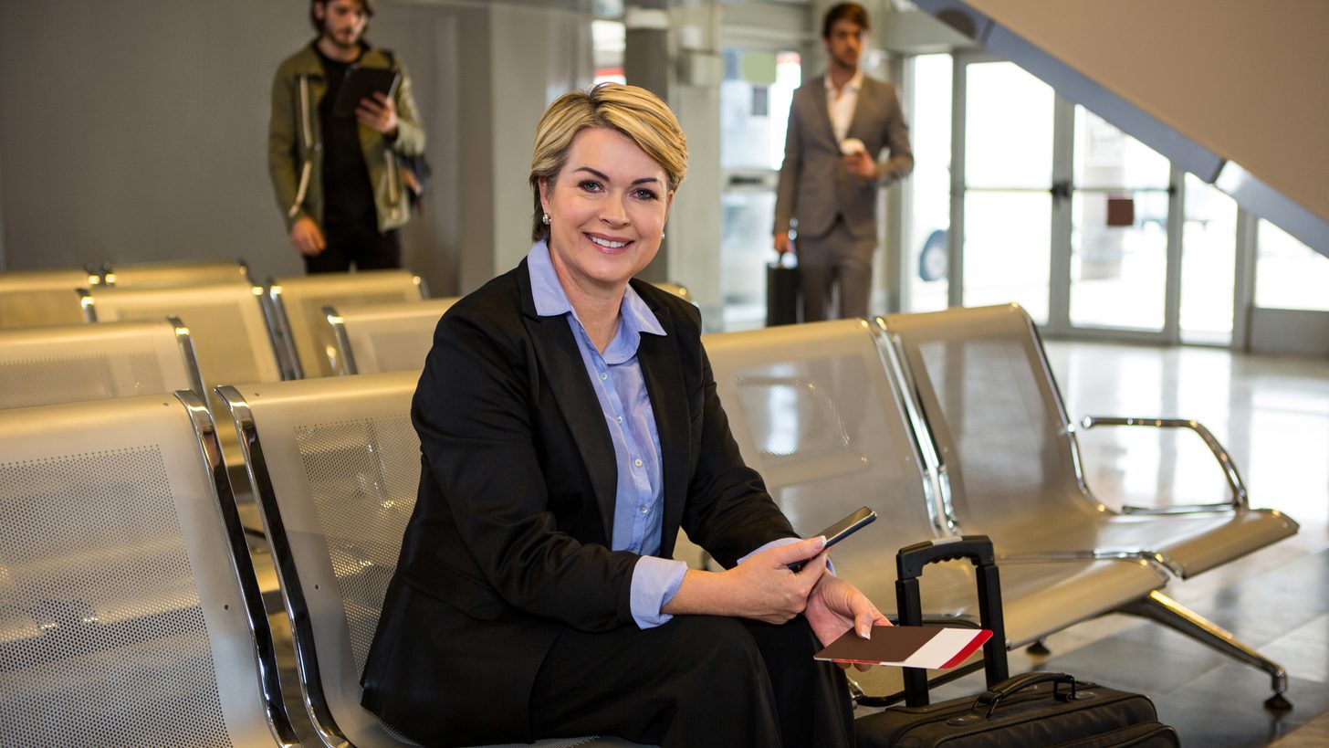 A traveller waiting in an airport departure area with passport and luggage