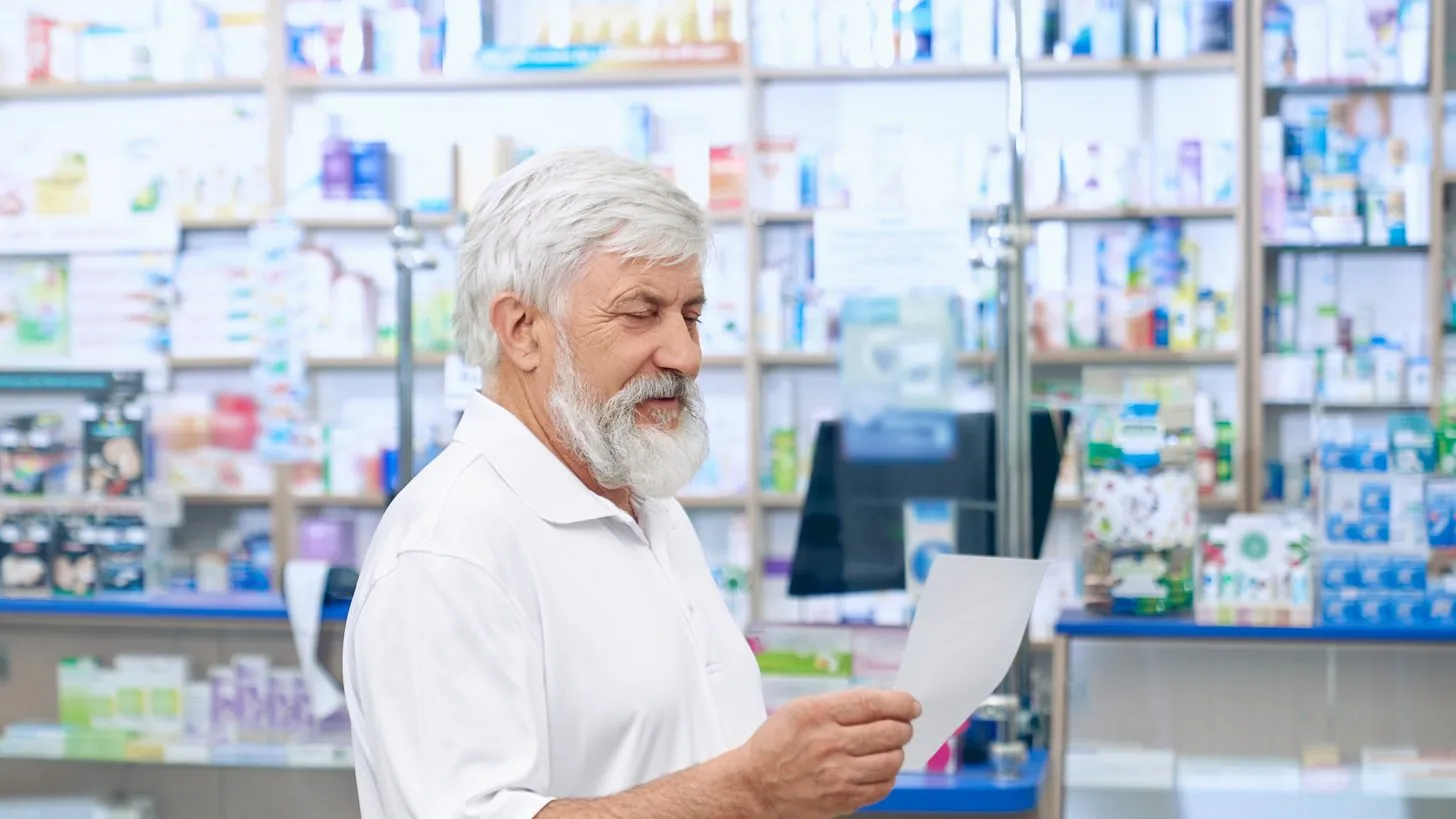 Eine reisende Person liest an einem Apothekentresen ein Rezept