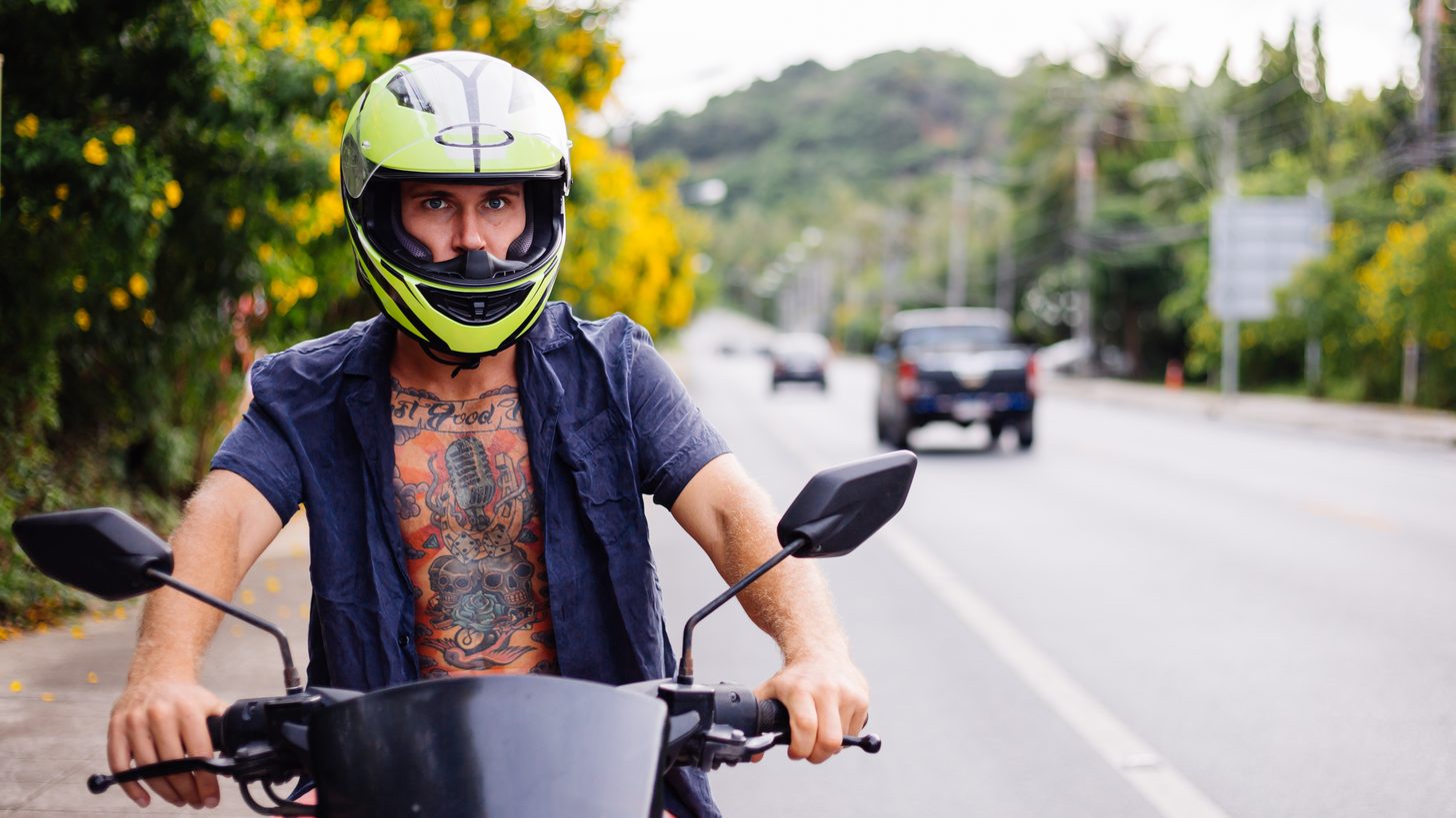 A rider in a helmet beside a motorbike on a Thai road