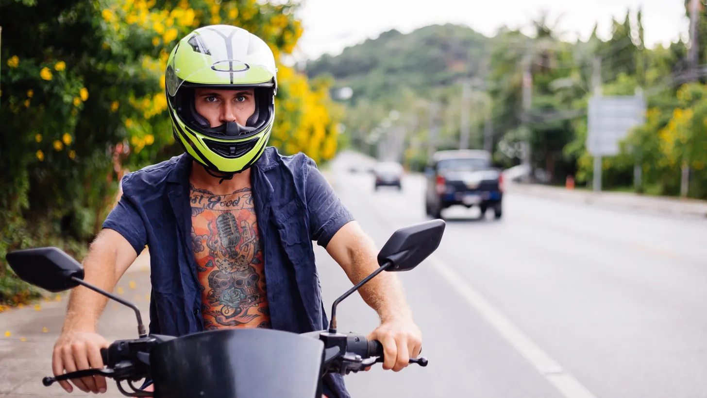 Ein Fahrer mit Helm neben einem Motorrad auf einer thailändischen Straße