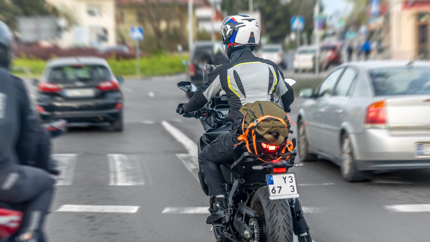 A motorcyclist in protective clothing waiting at a road intersection