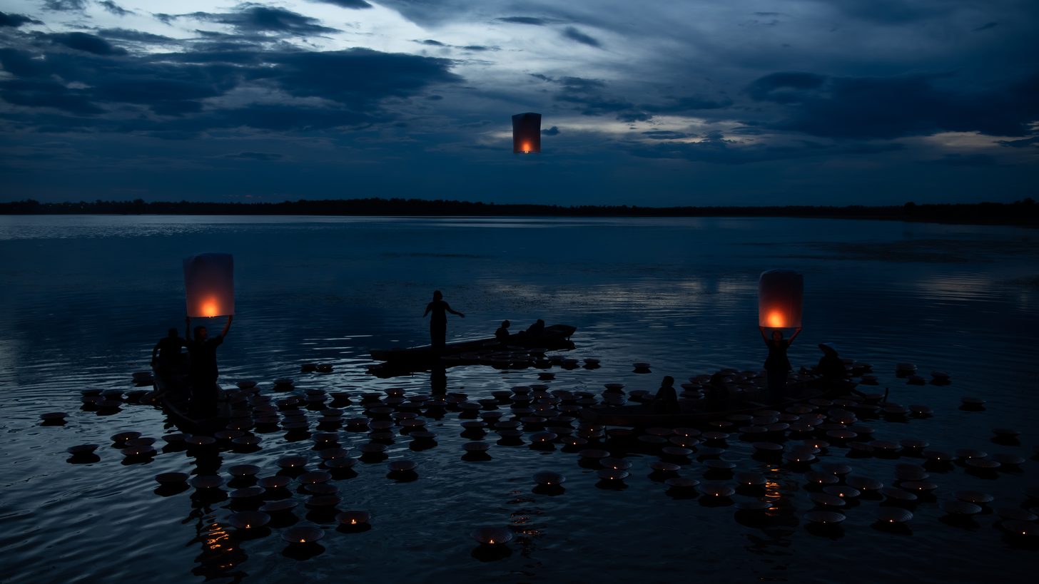 People floating decorated krathongs on the water at night