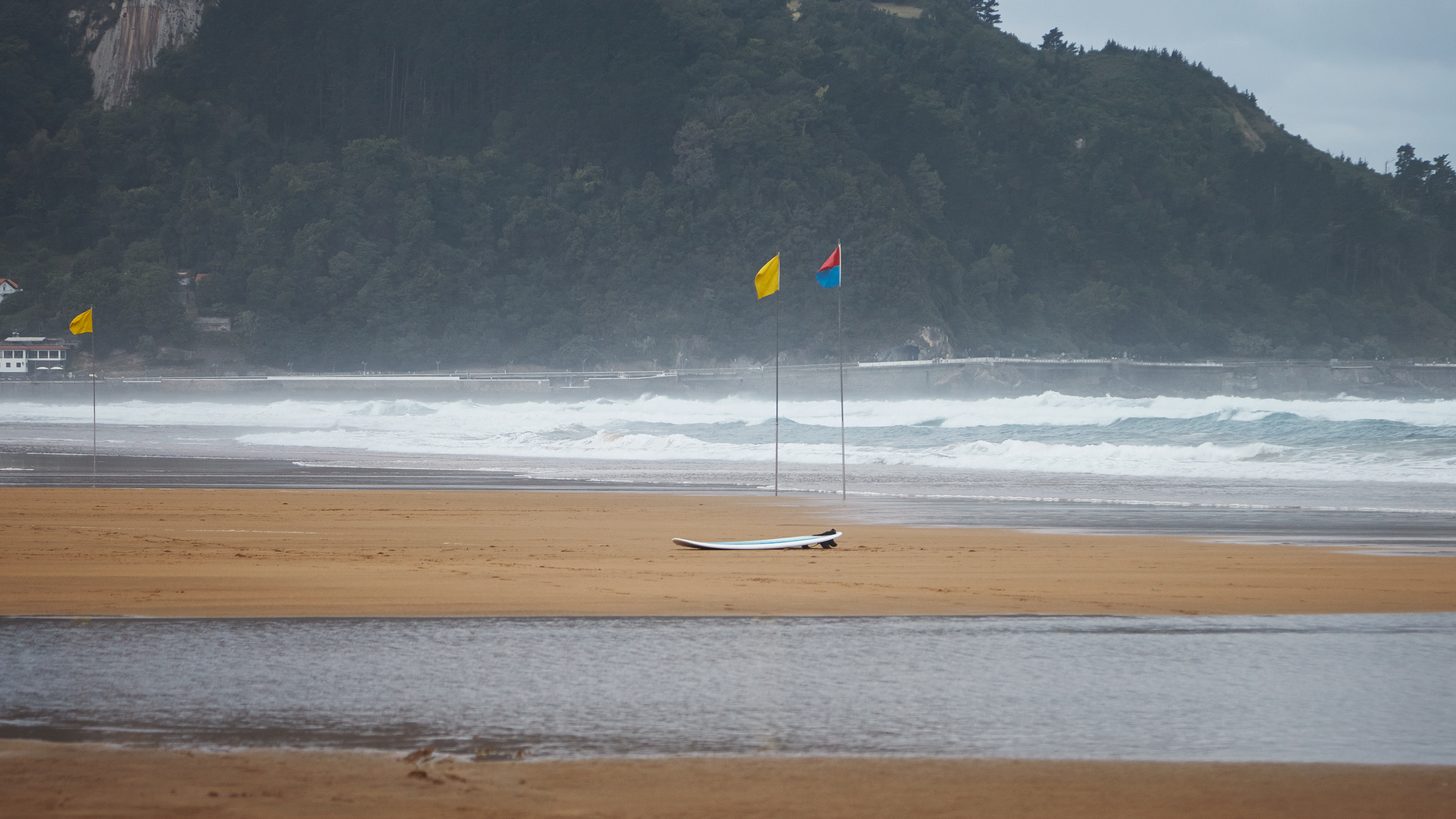 A red warning flag on a pole above a Thai beach with waves breaking behind it