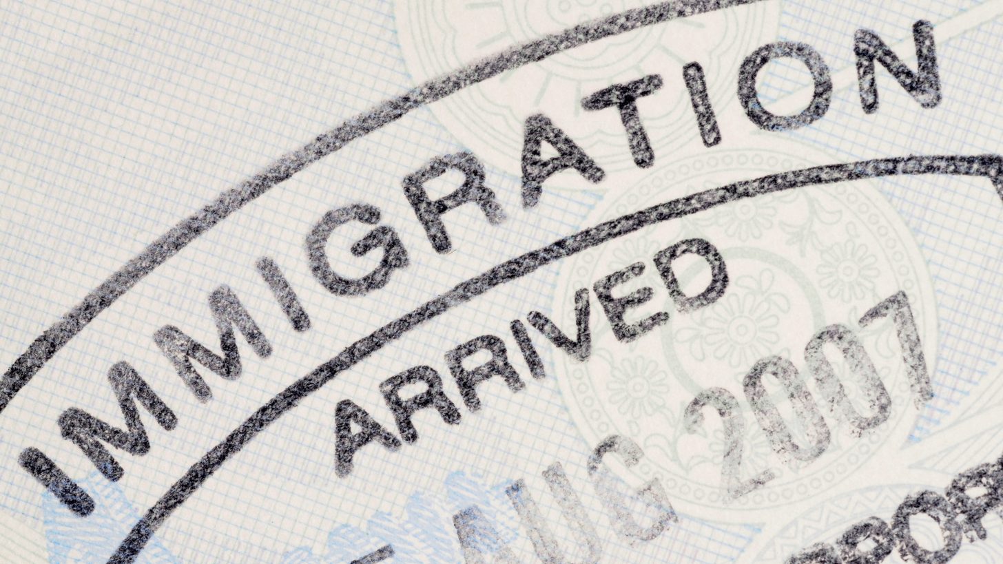 An immigration officer's desk with a passport being stamped at a border counter