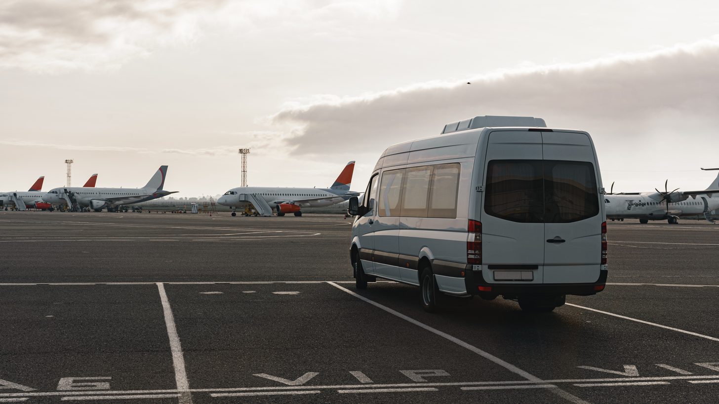 A minibus and driver waiting for passengers outside an arrivals terminal
