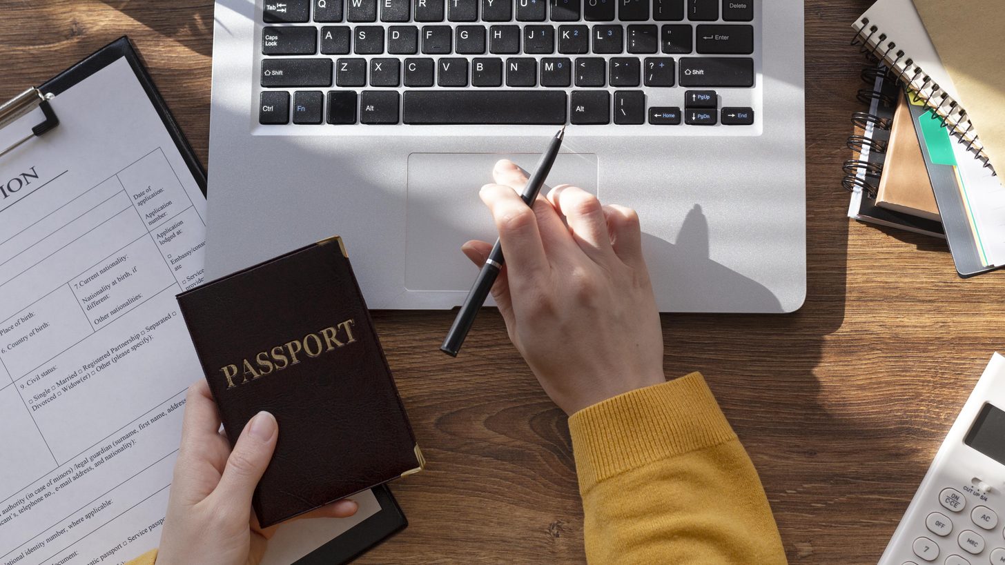 A passport held beside a laptop and a visa application form on a desk