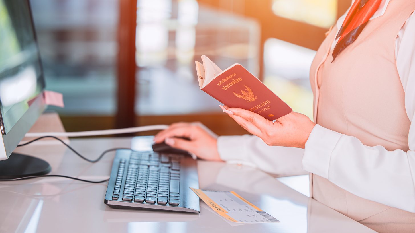 An airline check-in agent holding an open Thai passport at the counter