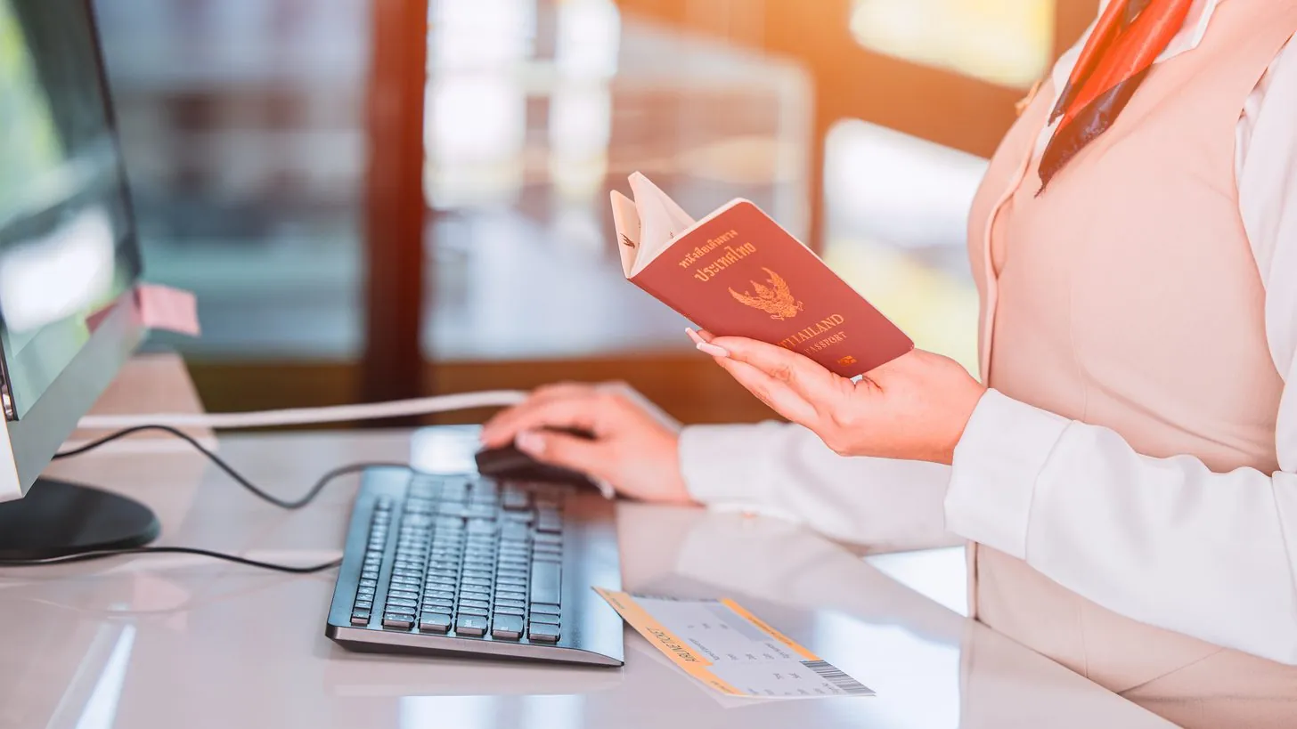Eine Check-in-Mitarbeiterin hält am Schalter einen aufgeschlagenen thailändischen Reisepass