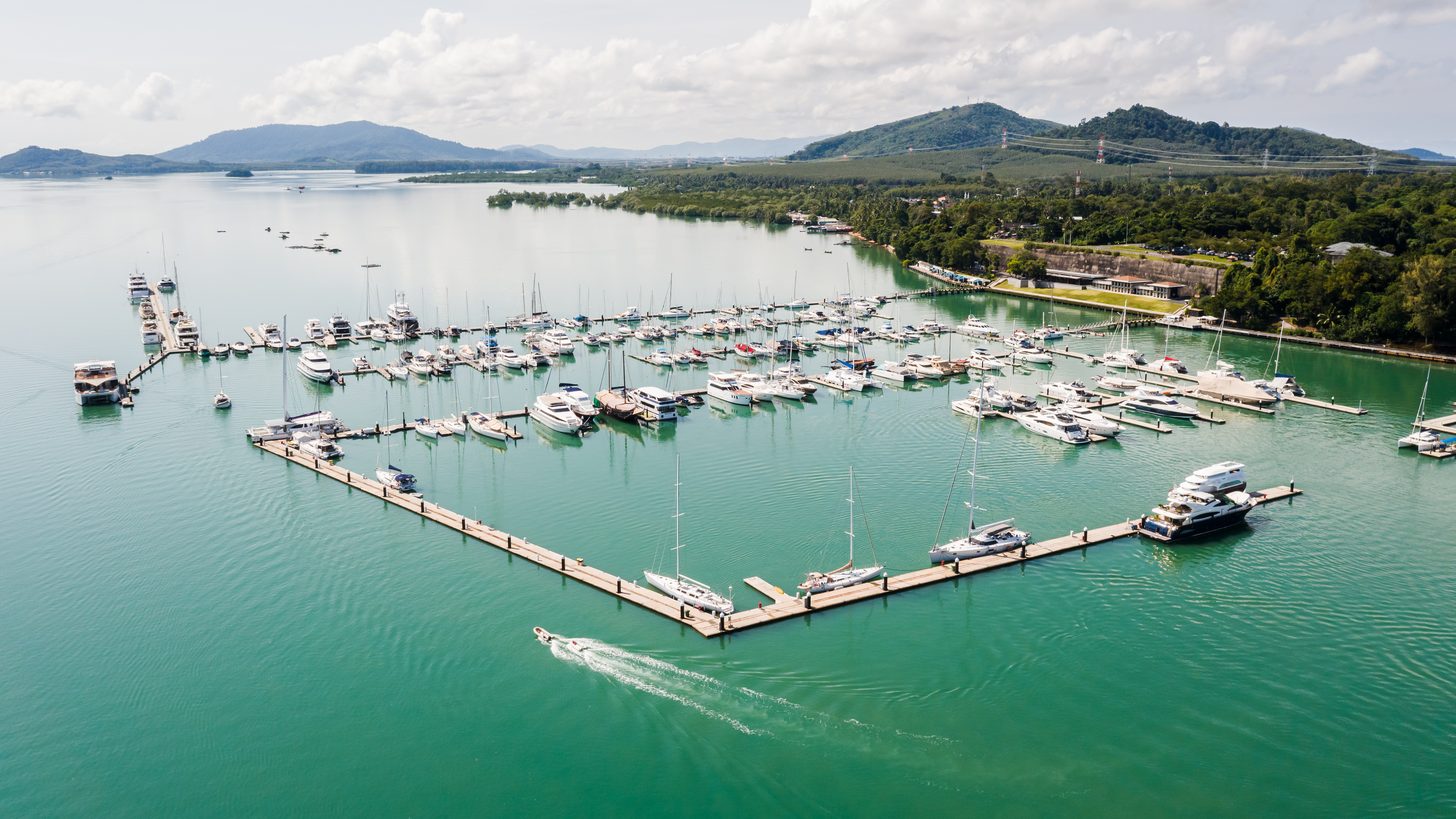 An aerial view of a yacht marina, rows of berths along floating pontoons on a green tropical coast