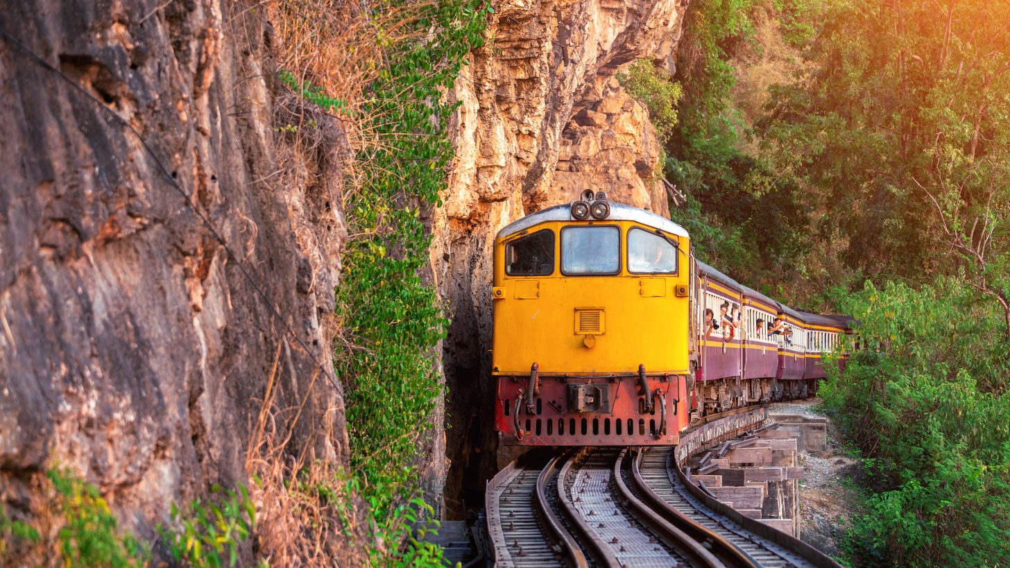 A Thai passenger train running on existing cliffside track in Kanchanaburi