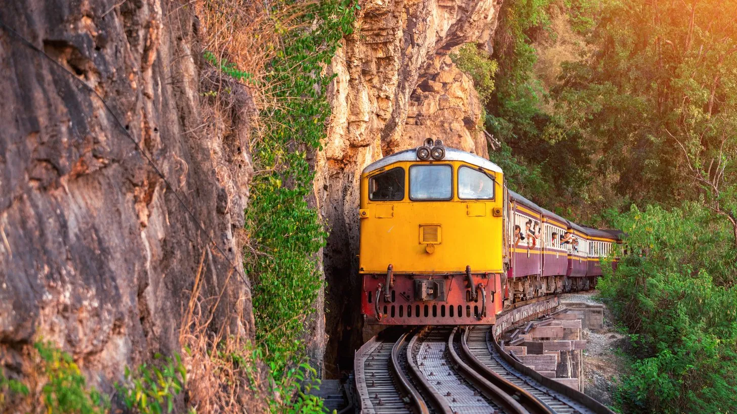 Ein thailändischer Personenzug auf der bestehenden Trasse an der Felswand bei Kanchanaburi