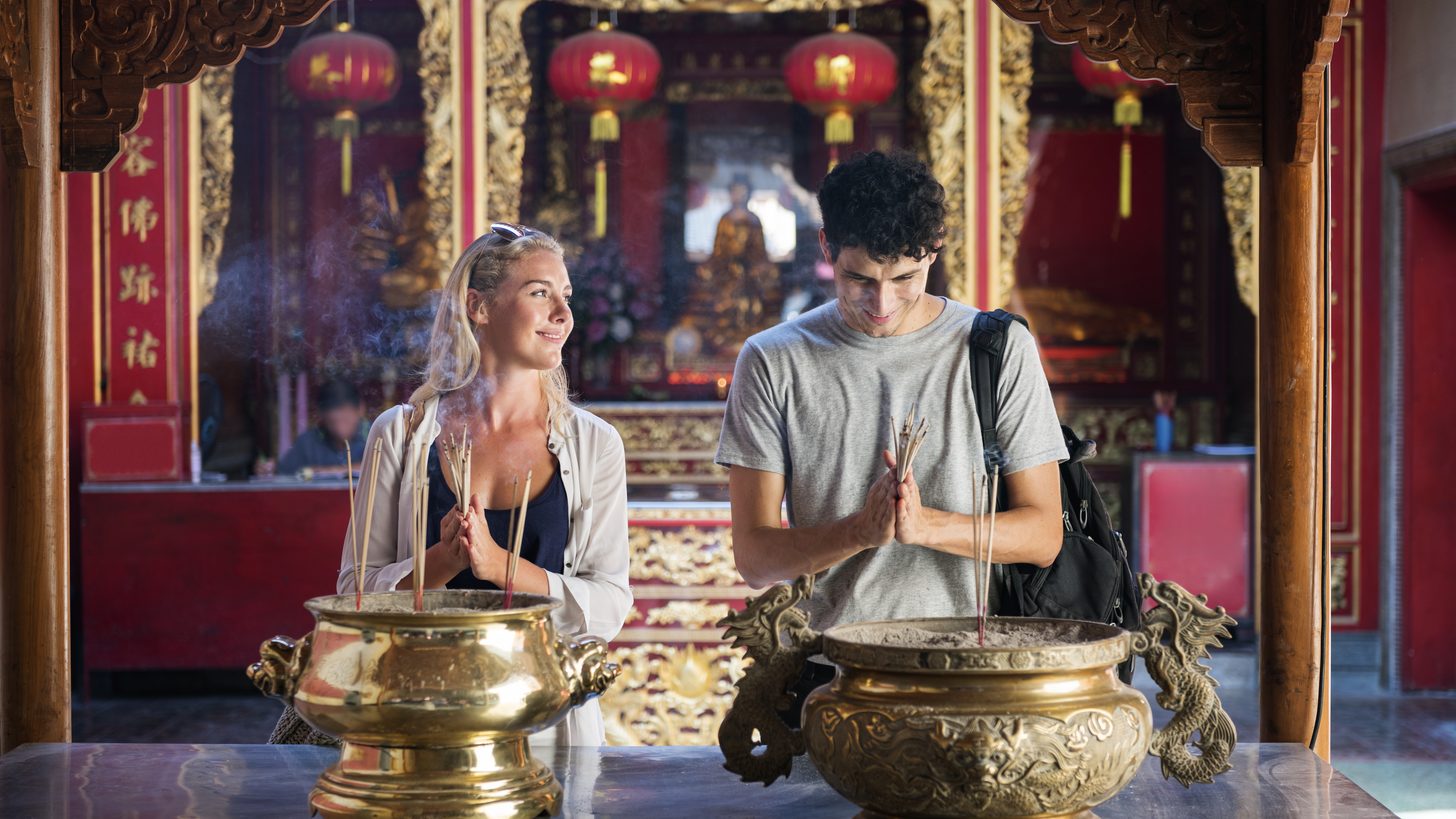 Two visitors holding incense with their hands pressed together at a temple shrine